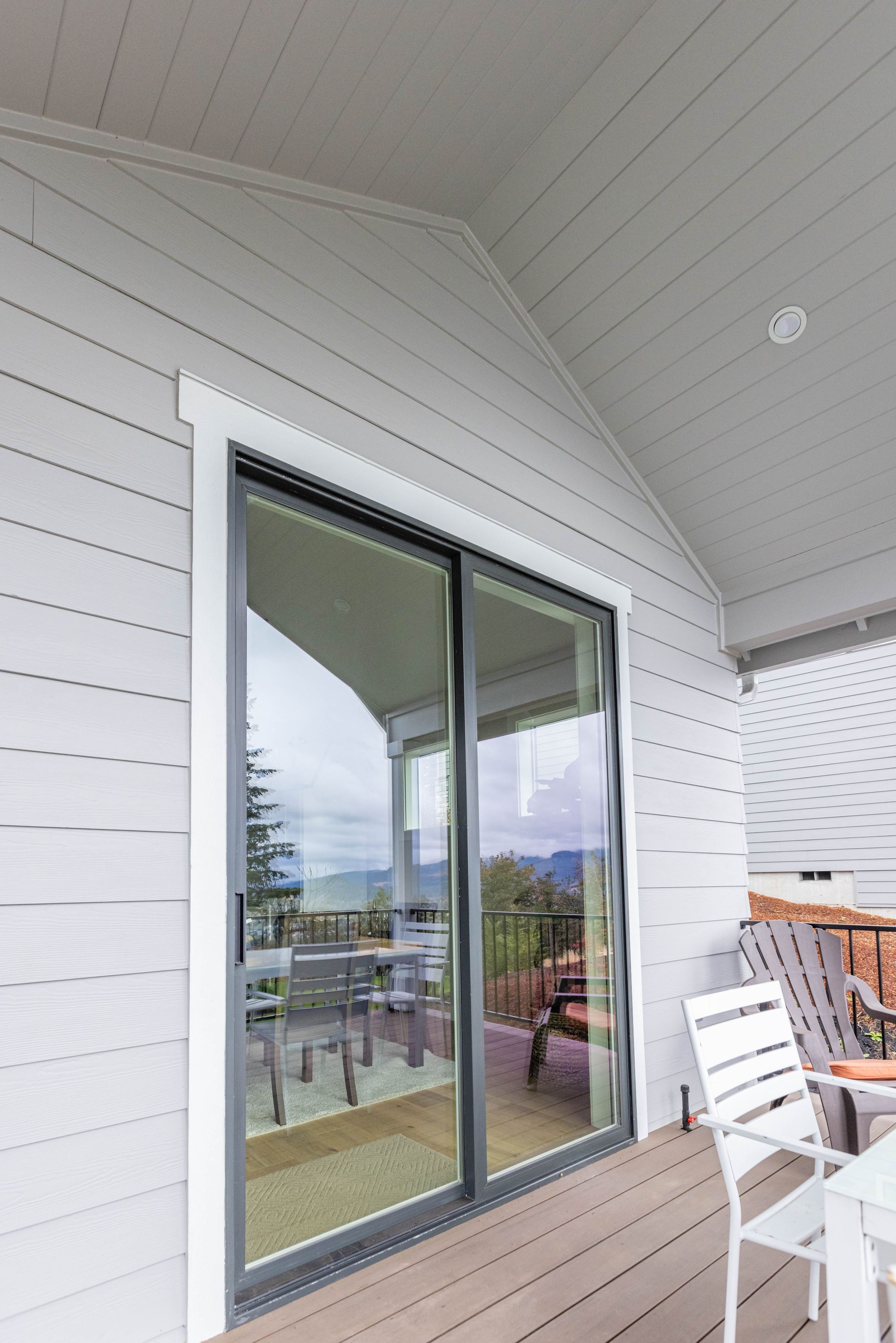 White balcony with sliding glass door, outdoor chairs, and a view of mountains and water