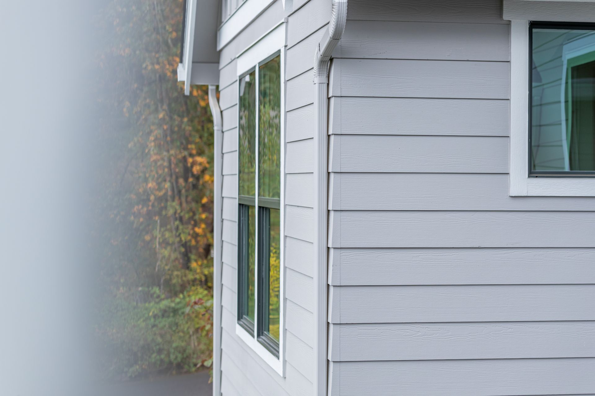 Gray-sided house exterior with white-trimmed windows, partly blurred by mist or rain