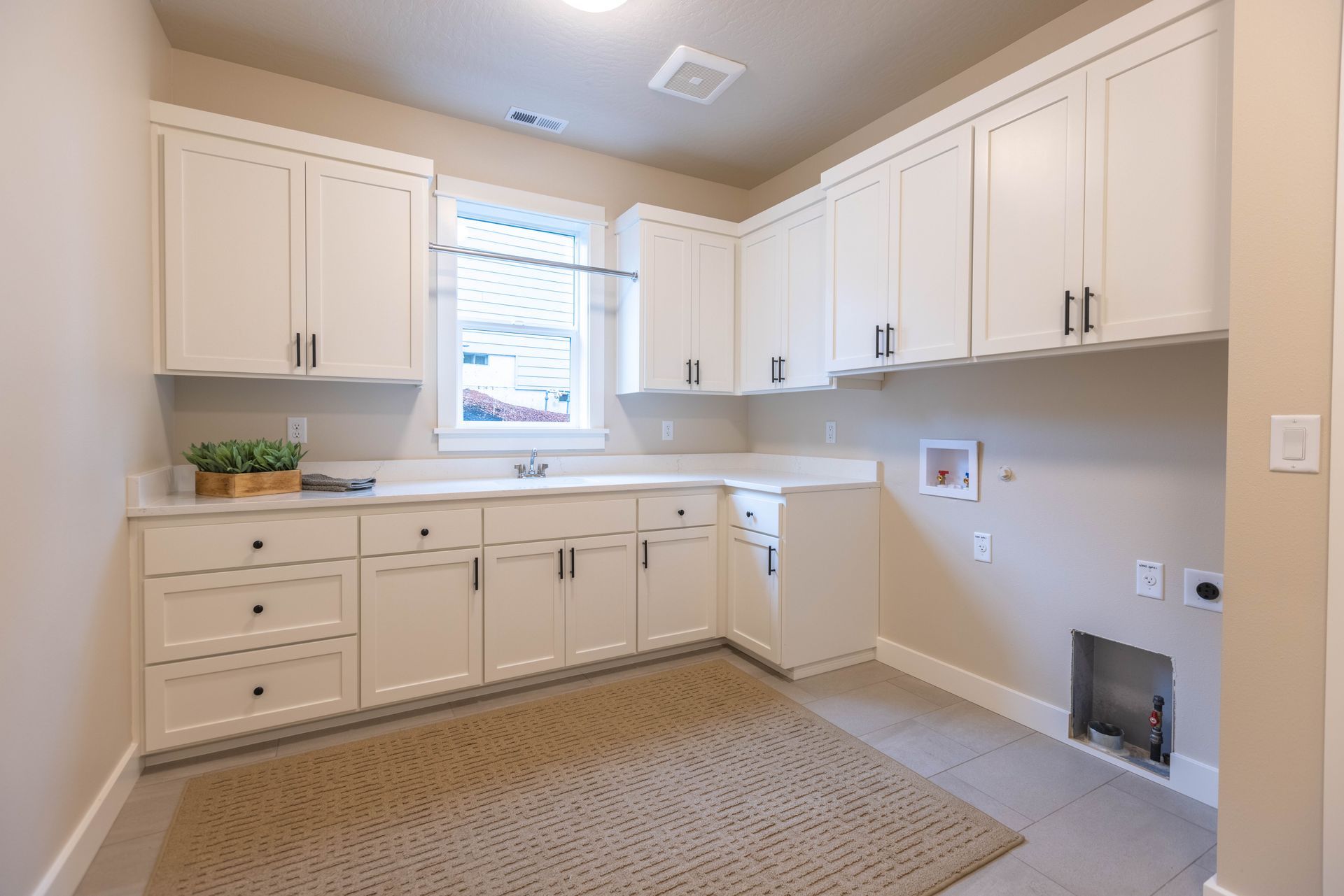 Bright white kitchen with cabinets, window, beige countertops, and a patterned rug