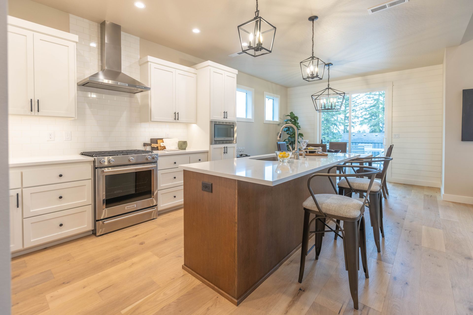 Bright modern kitchen with white cabinets, wood island, pendant lights, and dining table by a window