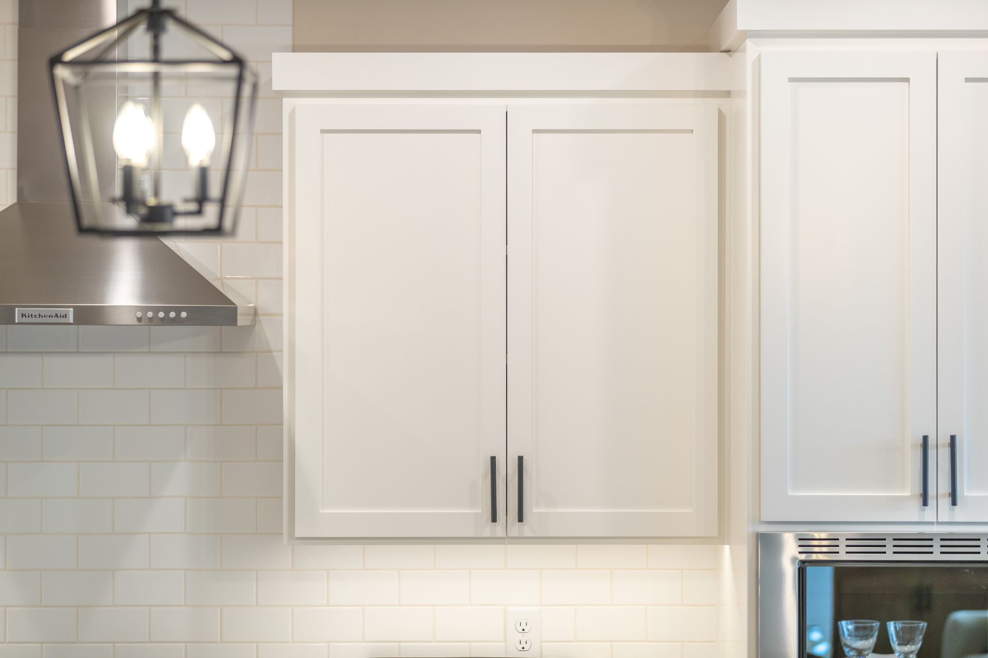 White kitchen cabinets and a hanging lantern-style light over a tiled backsplash.