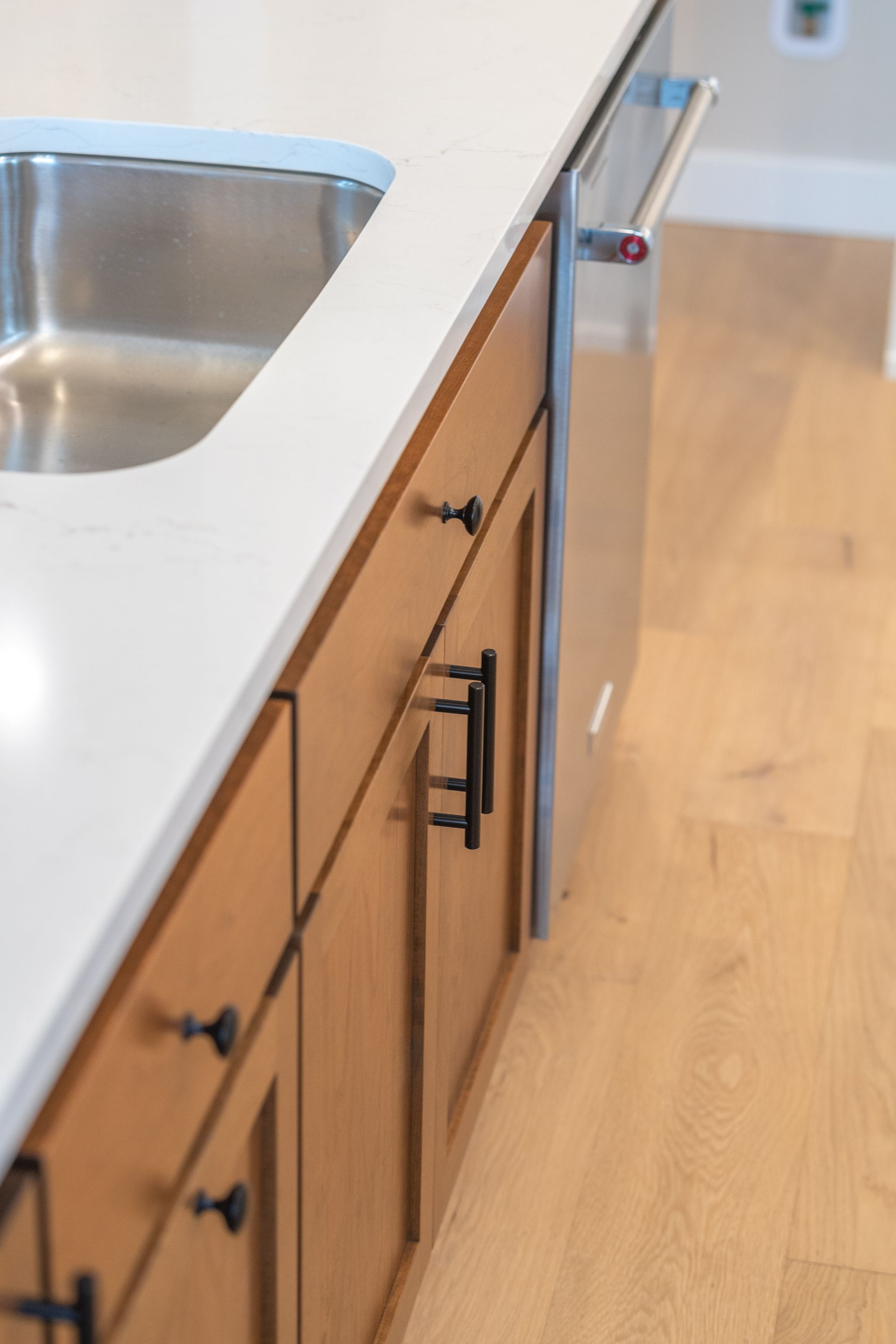 Kitchen island with white countertop, stainless sink, wood cabinets, and built-in appliances on a hardwood floor