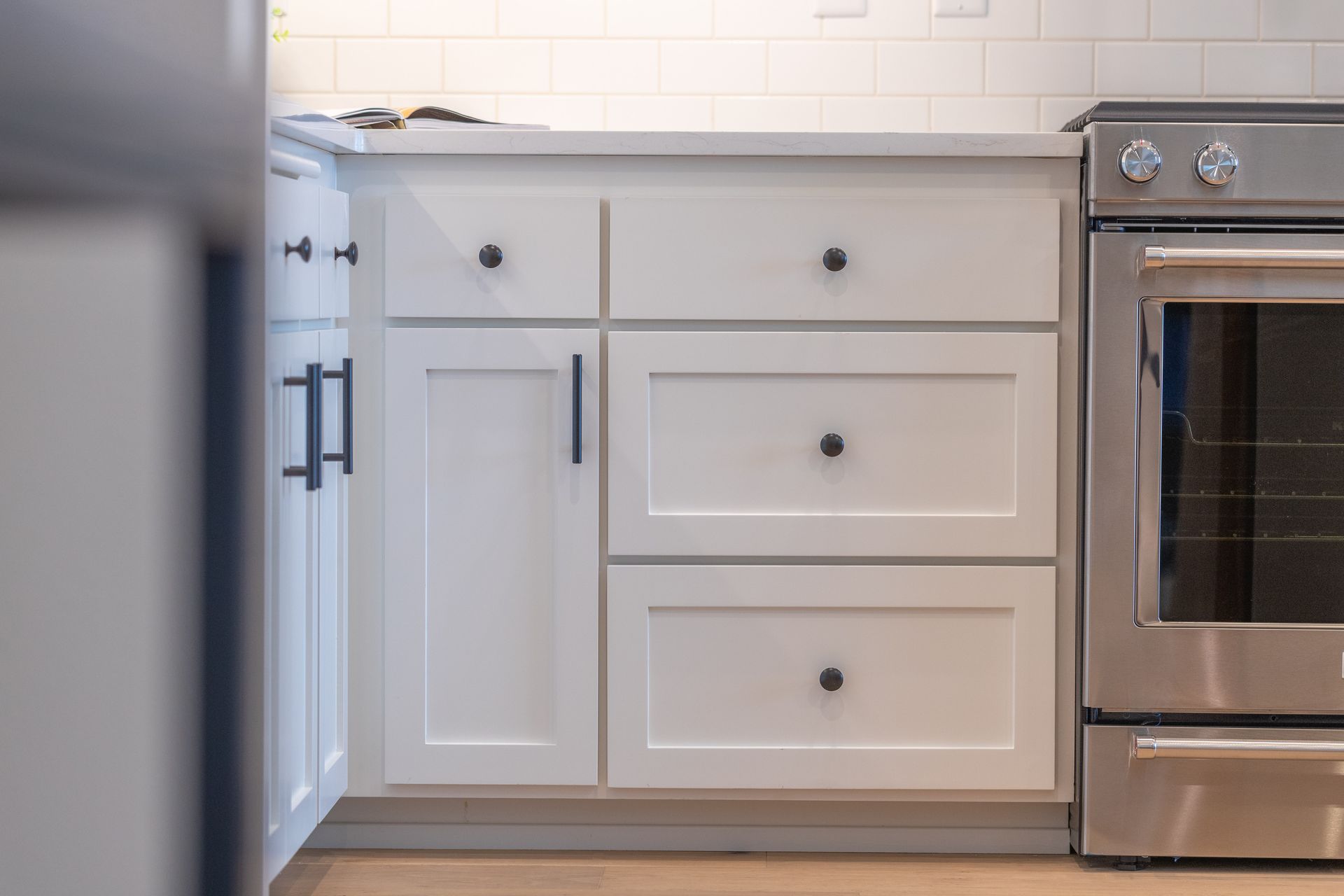 White kitchen cabinets with drawers beside a stainless steel oven and dishwasher under a tiled backsplash