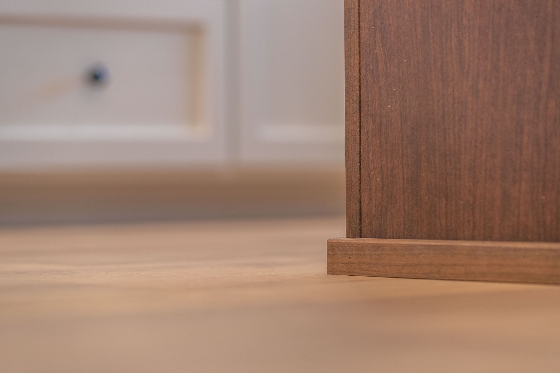 Close-up of a wooden cabinet edge on a light floor, with a blurred drawer in the background