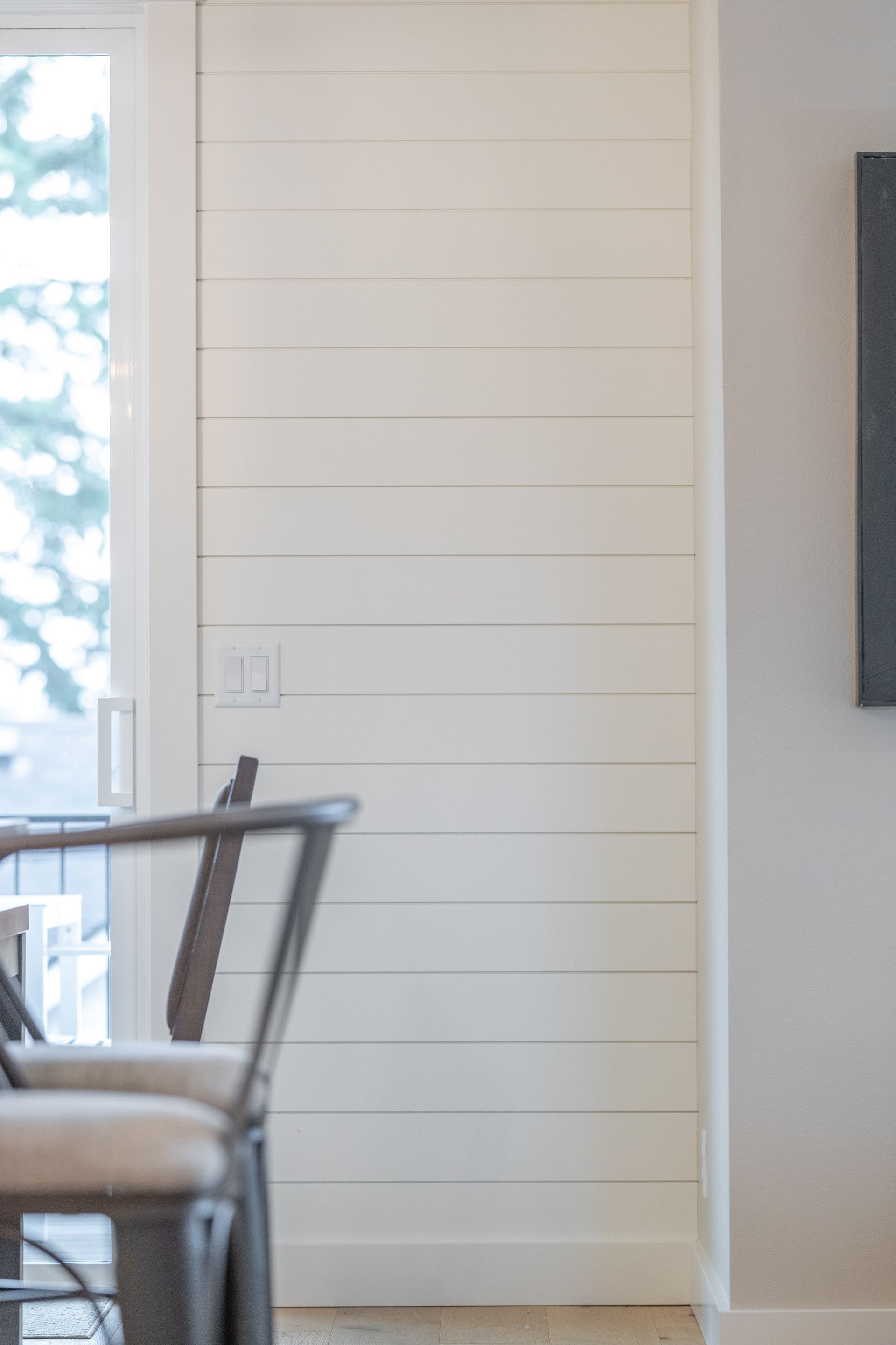 Bright white shiplap wall beside a dining chair and window in a sunlit room