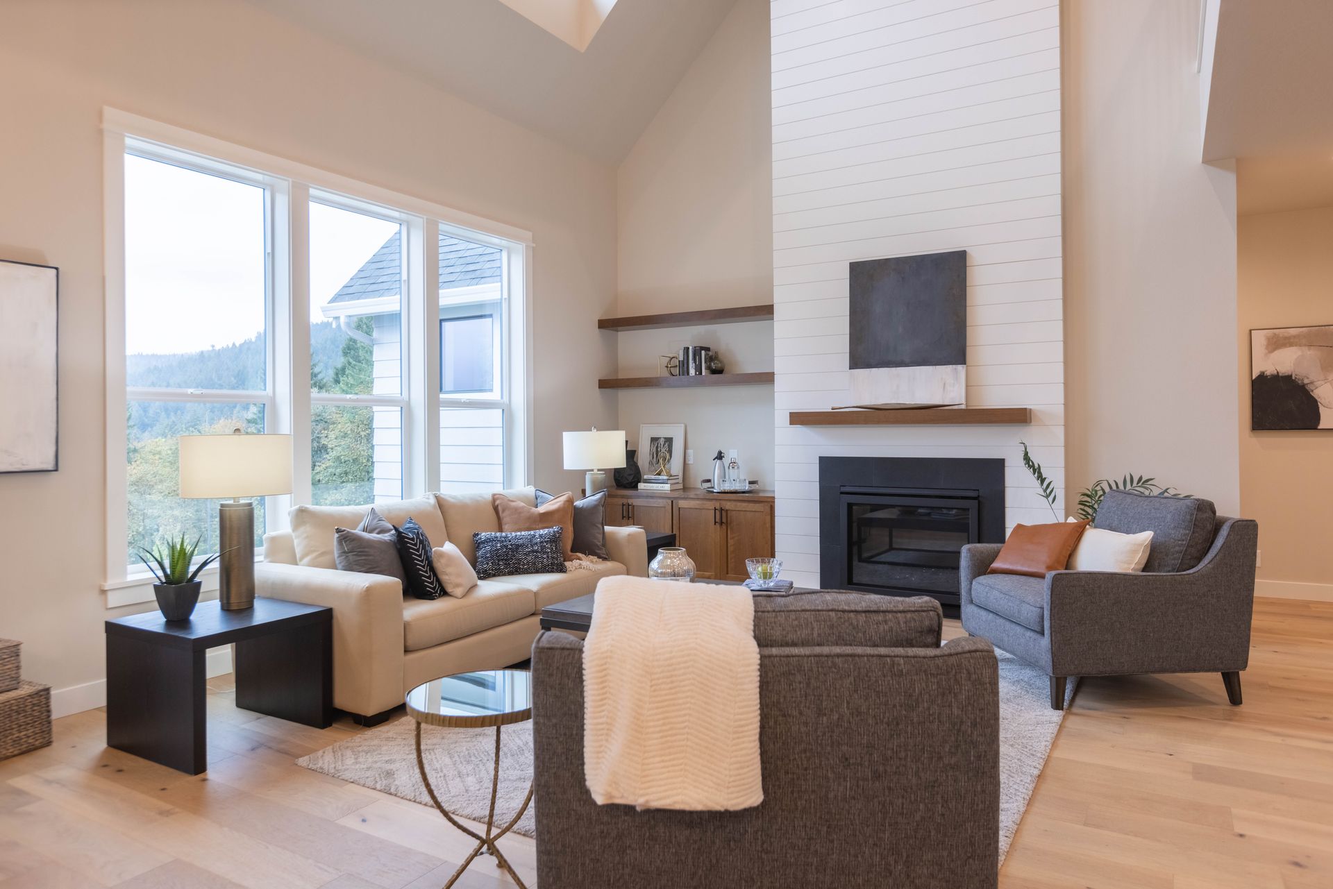 Bright modern living room with fireplace, large windows, and gray sofas around a coffee table