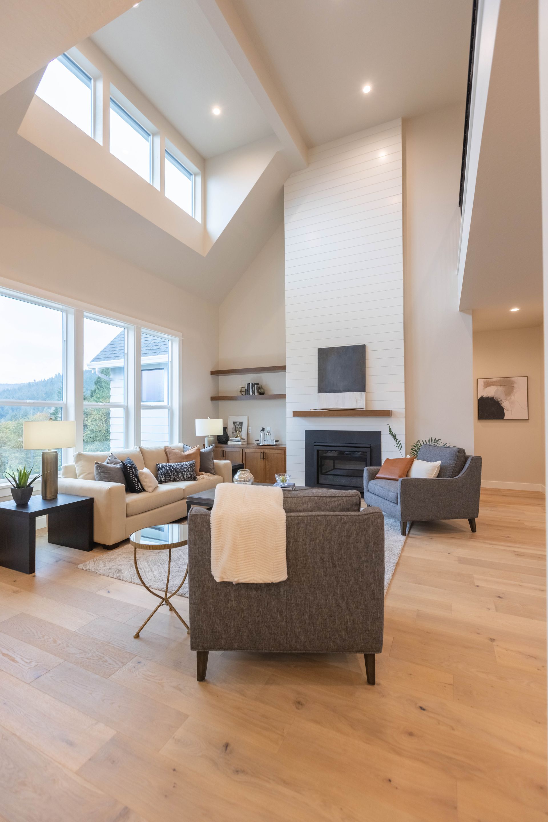Bright modern living room with tall windows, fireplace, and gray chairs on a wood floor