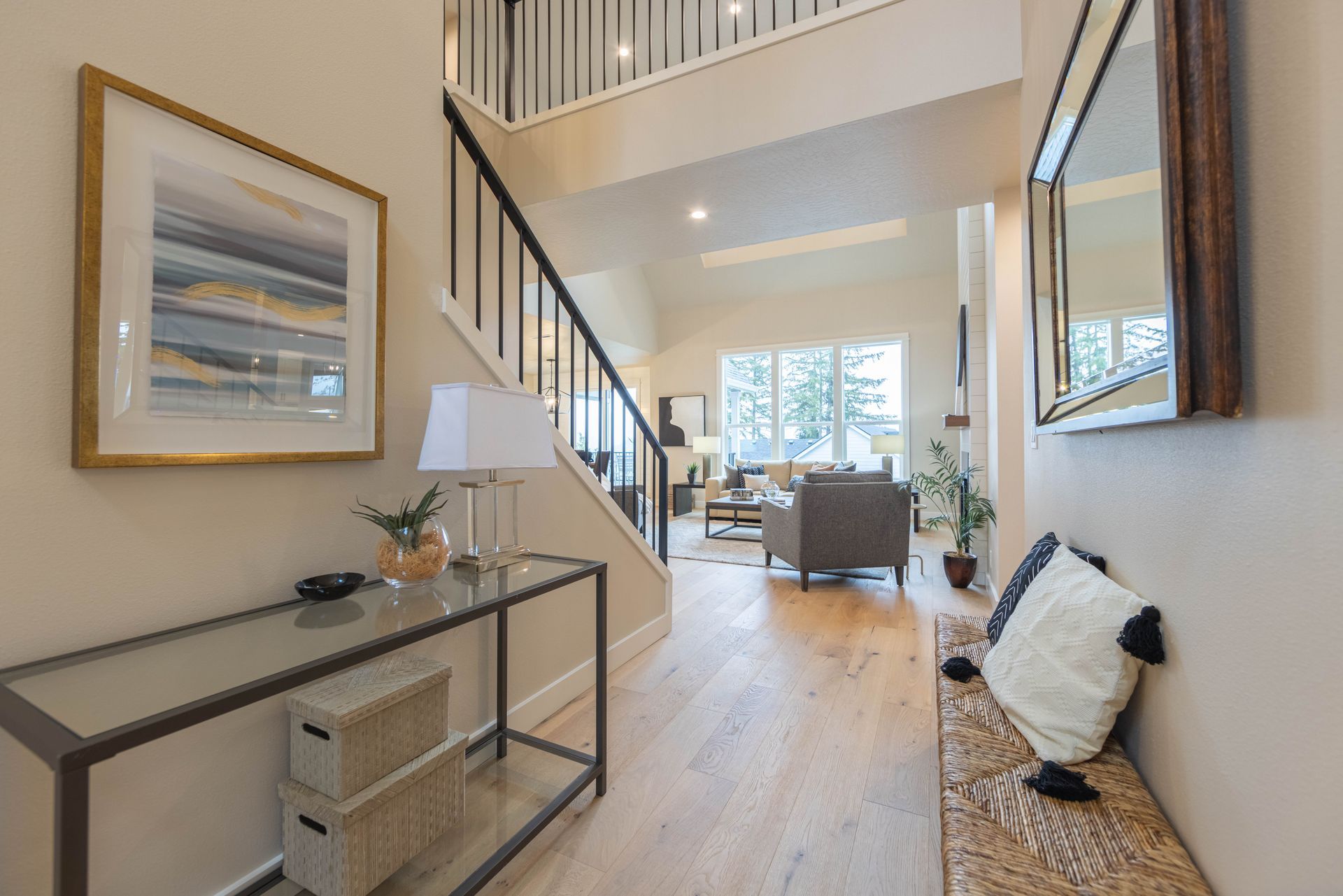 Bright entry hall with staircase, console table, bench, and open view into a sunlit living room