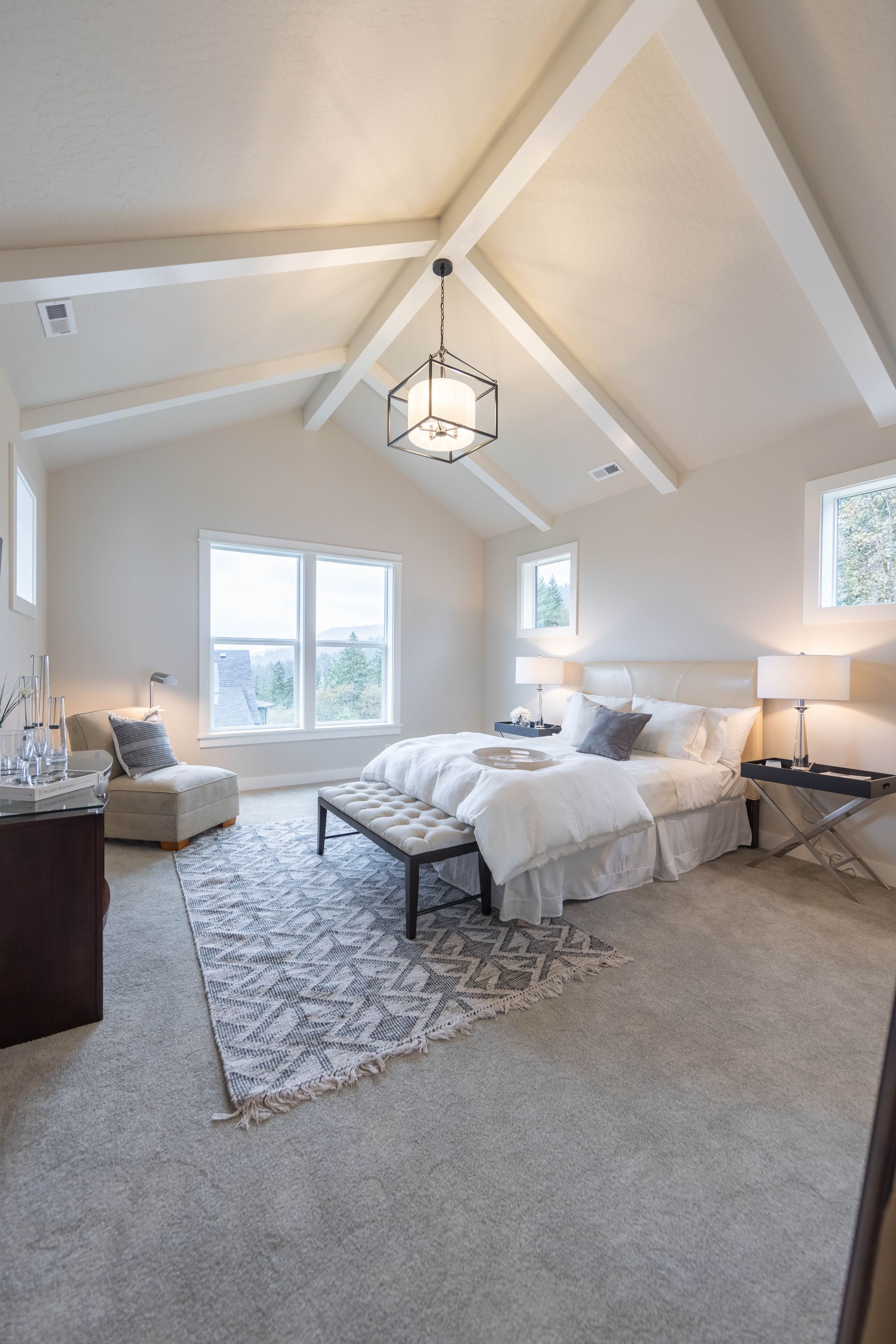 Bright vaulted bedroom with white bedding, gray rug, and chandelier in a cozy neutral space