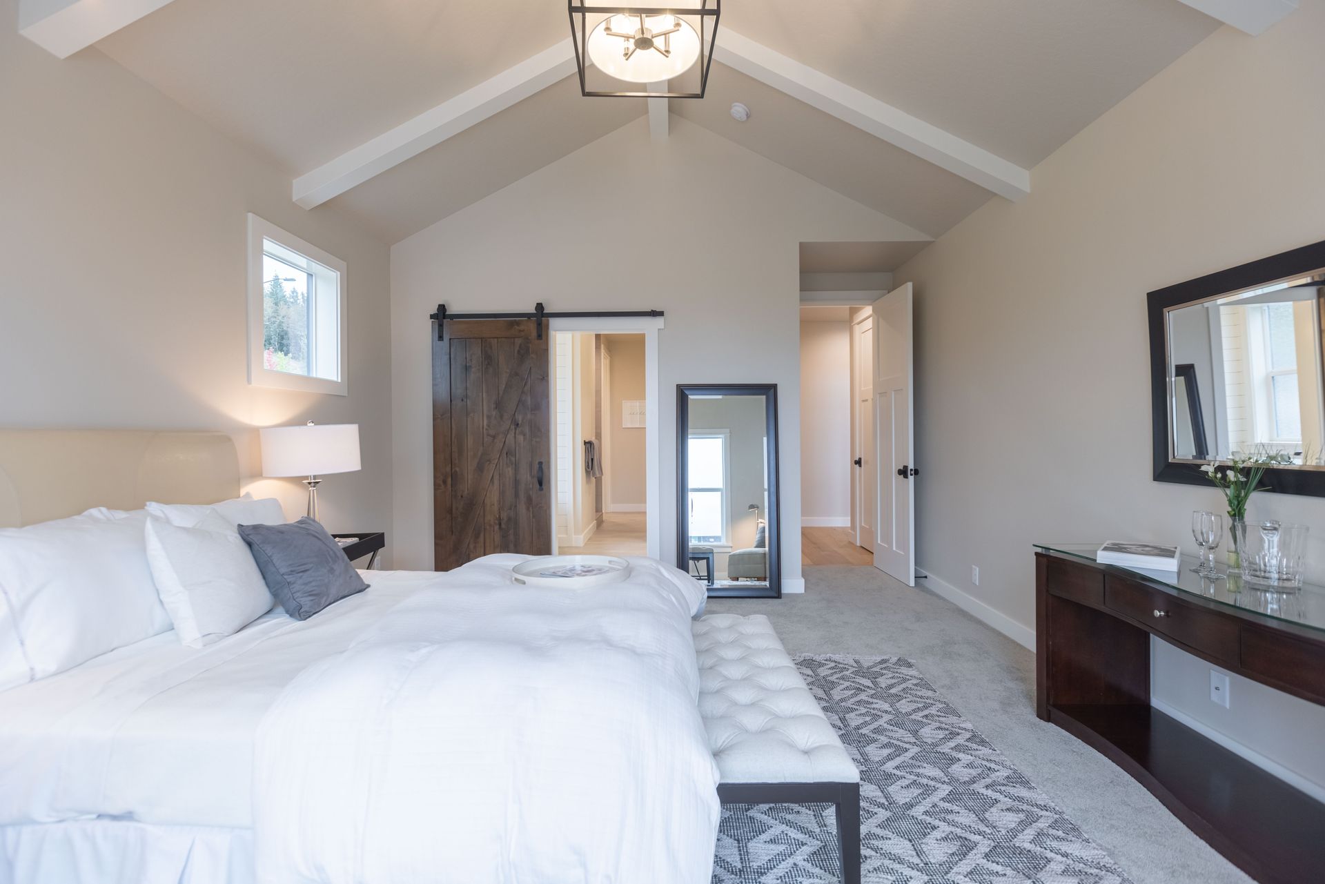 Spacious bedroom with vaulted ceiling, white bed, patterned rug, and dark wood dresser.