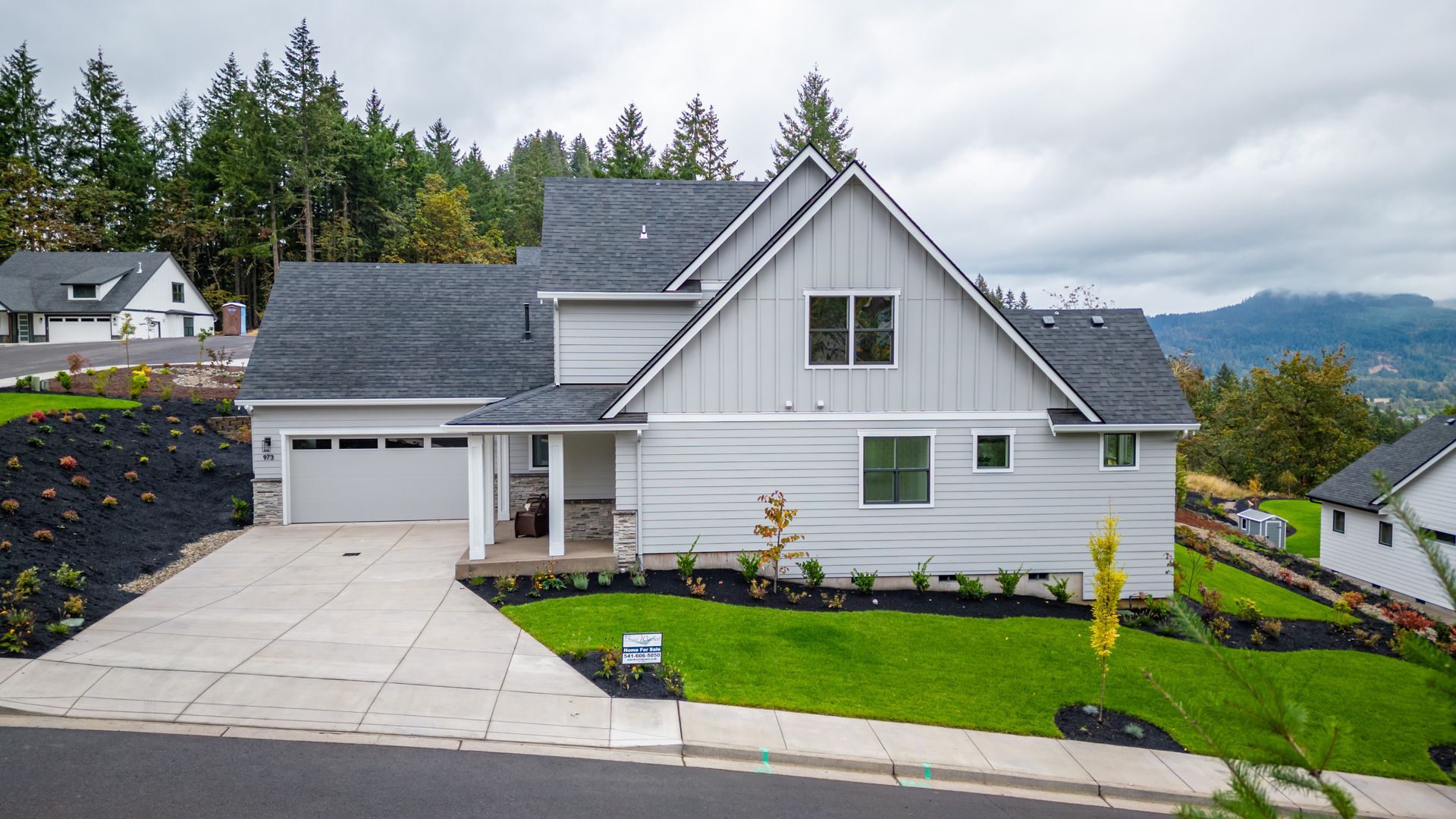 White suburban house with gray roof, driveway, and landscaped lawn overlooking trees and distant hills