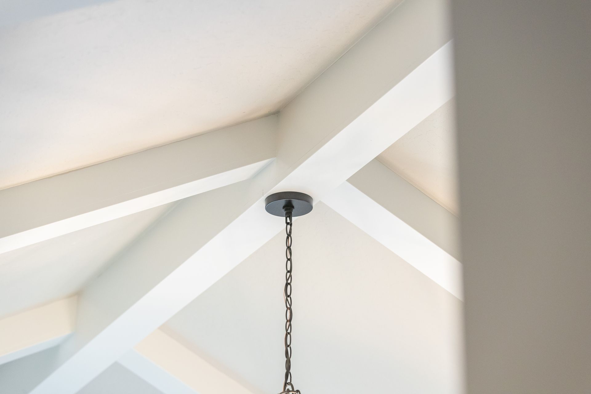 White vaulted ceiling with exposed beams and a hanging pendant light chain