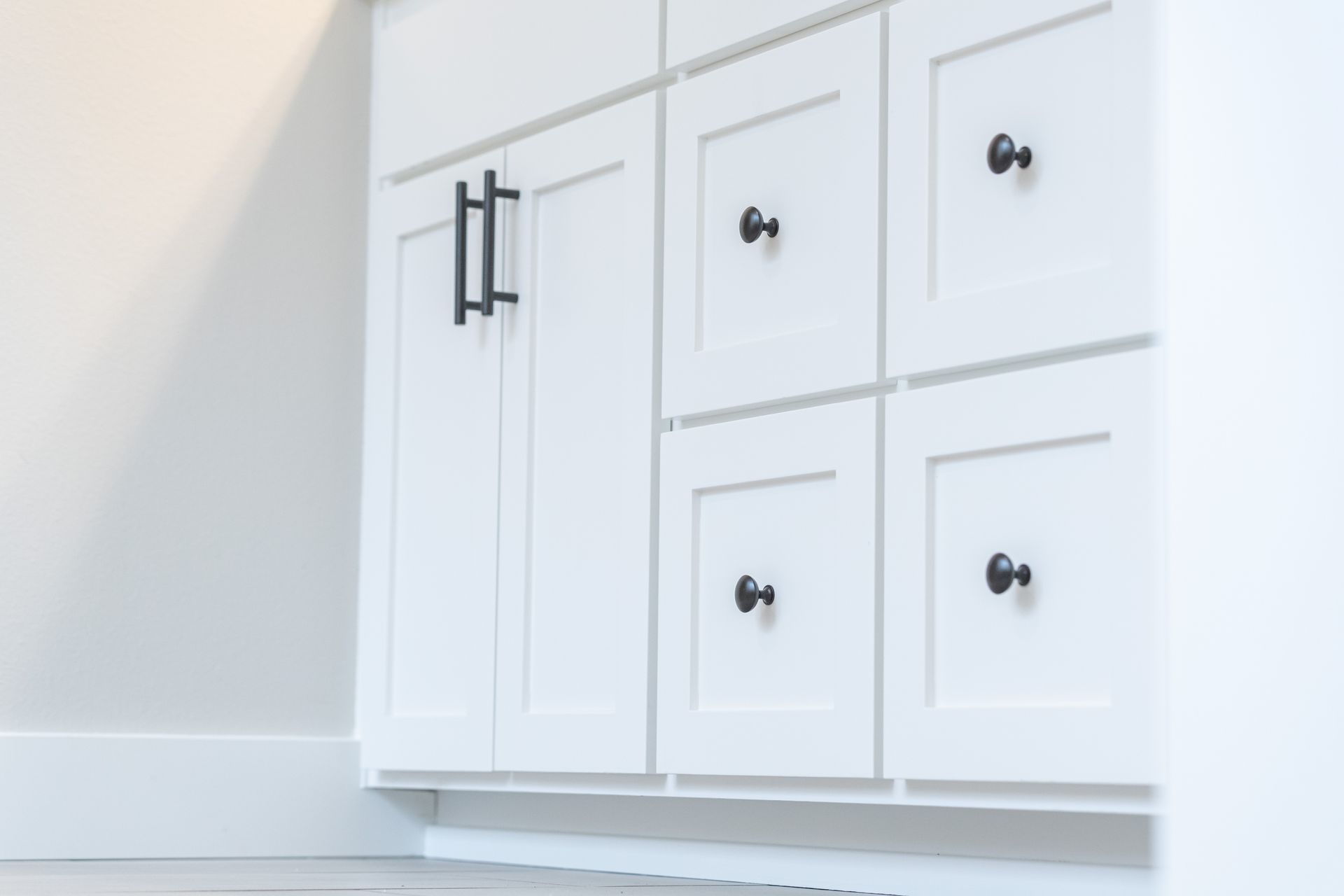 White bathroom vanity cabinet with black handles and four drawers, set against a light wall