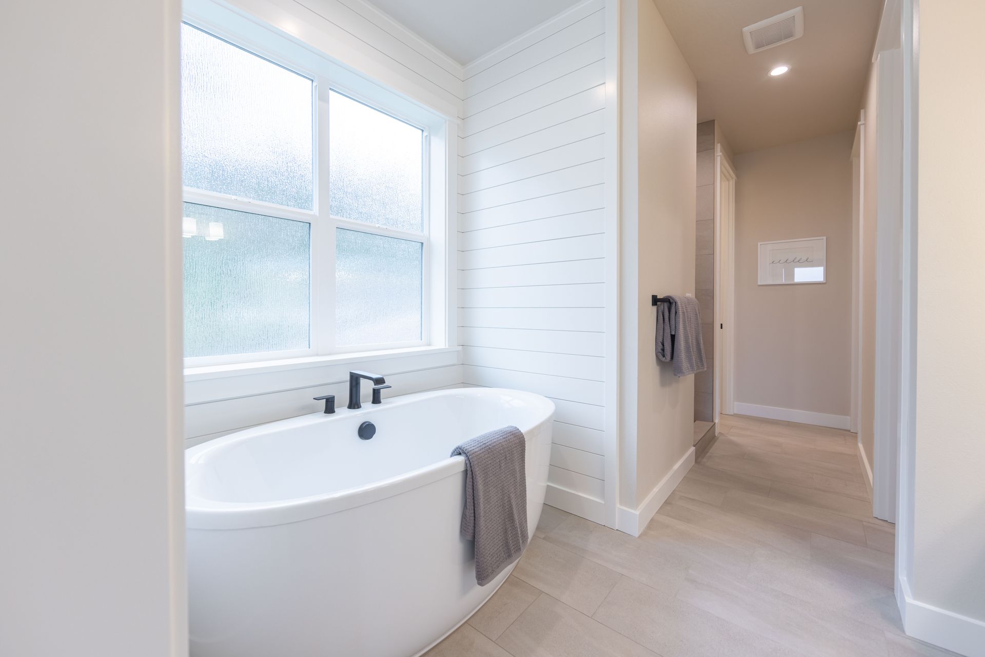 Bright modern bathroom with a freestanding tub, large window, and neutral tile floors