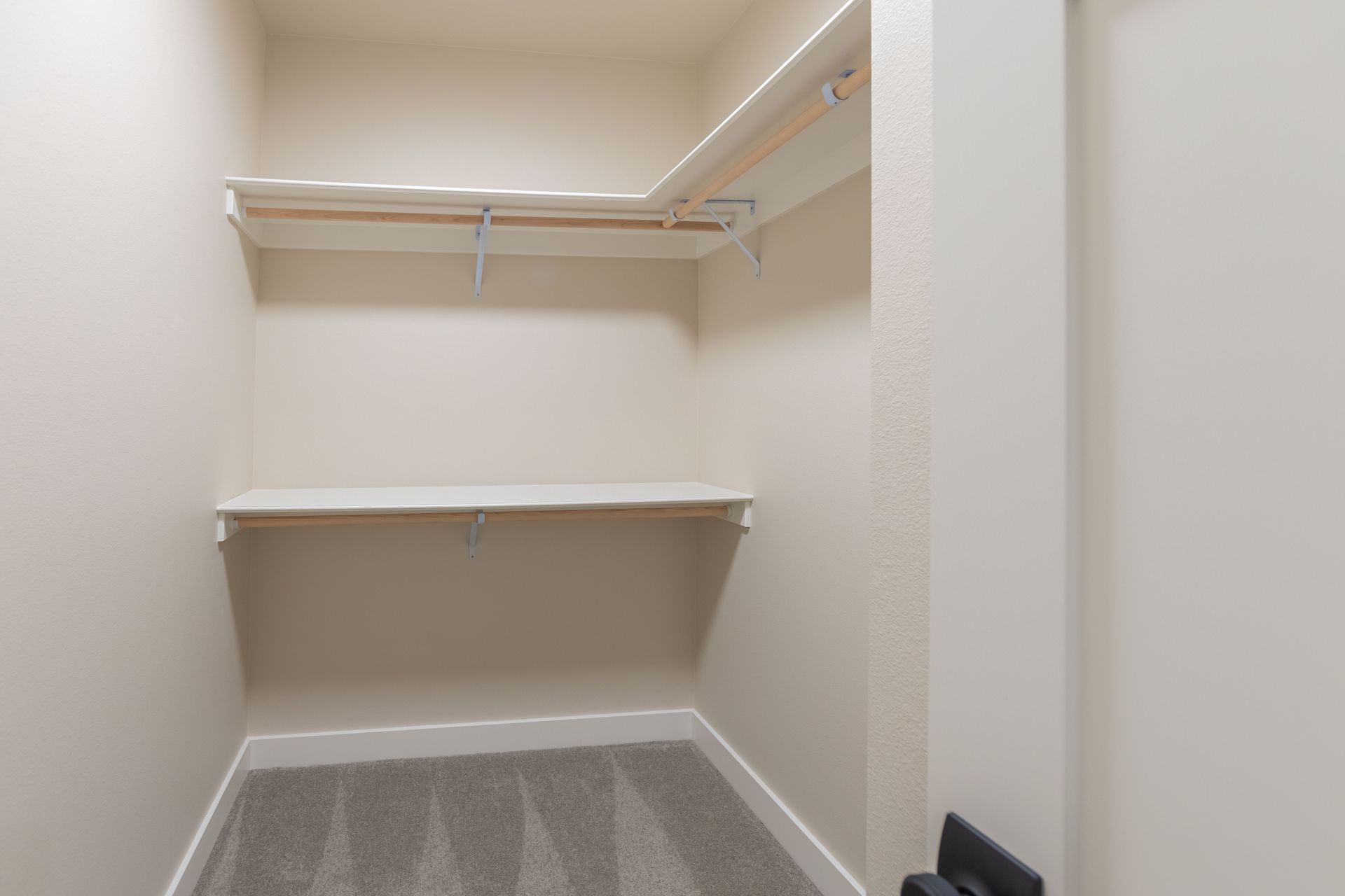 Empty walk-in closet with white wire shelves and beige walls, carpeted floor.