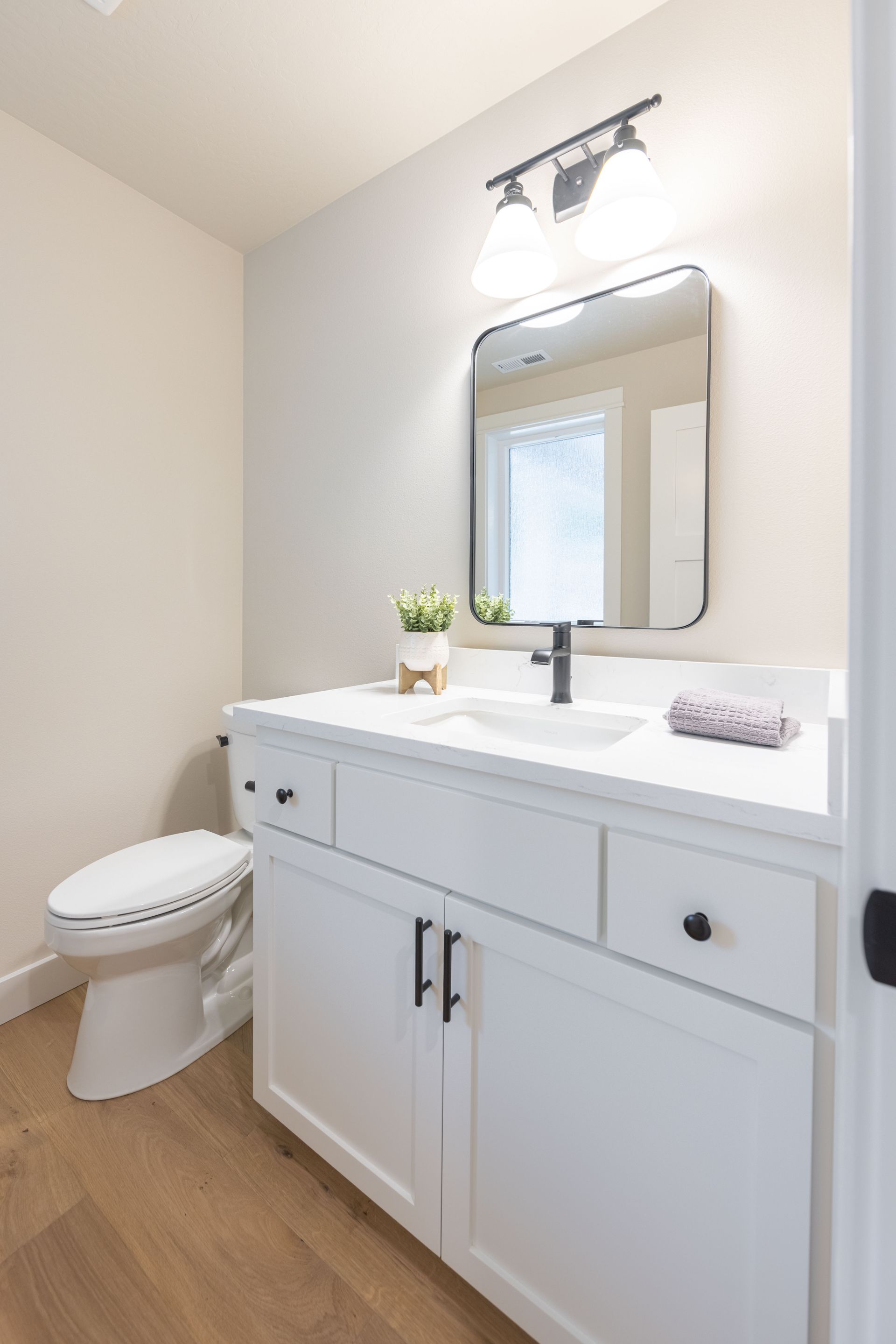 Bright bathroom vanity with white cabinets, mirror, sink, and toilet beside it.