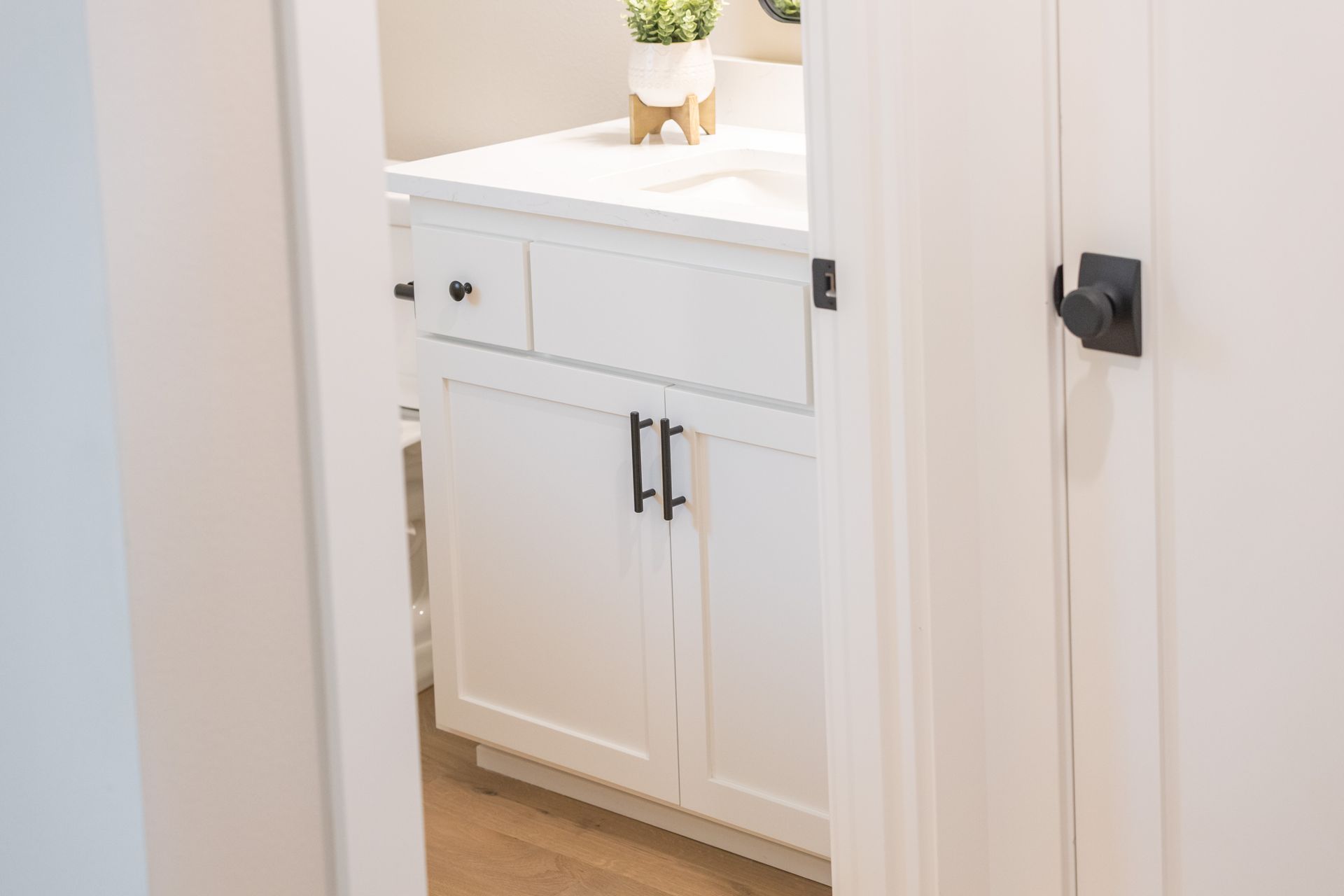 White bathroom vanity with cabinet doors and a countertop sink, seen through a doorway.