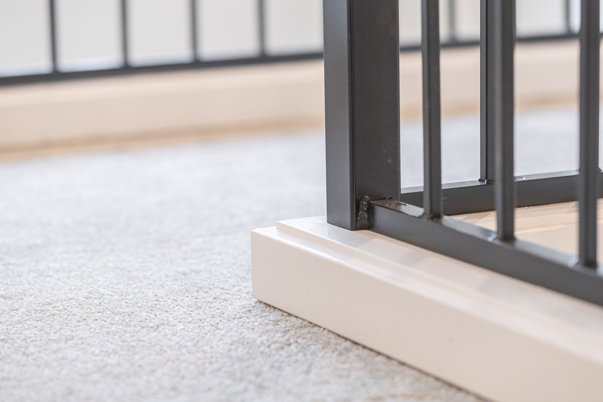 Gray metal gate on a white base over a light carpeted floor.