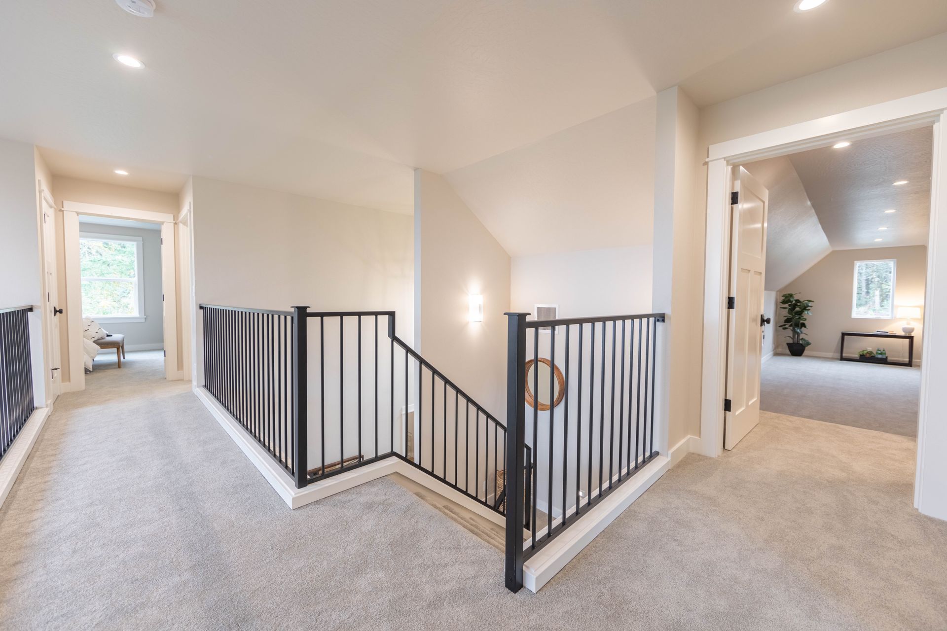 Bright upstairs hallway with black railing, carpeted stairs, and a doorway into a bedroom.