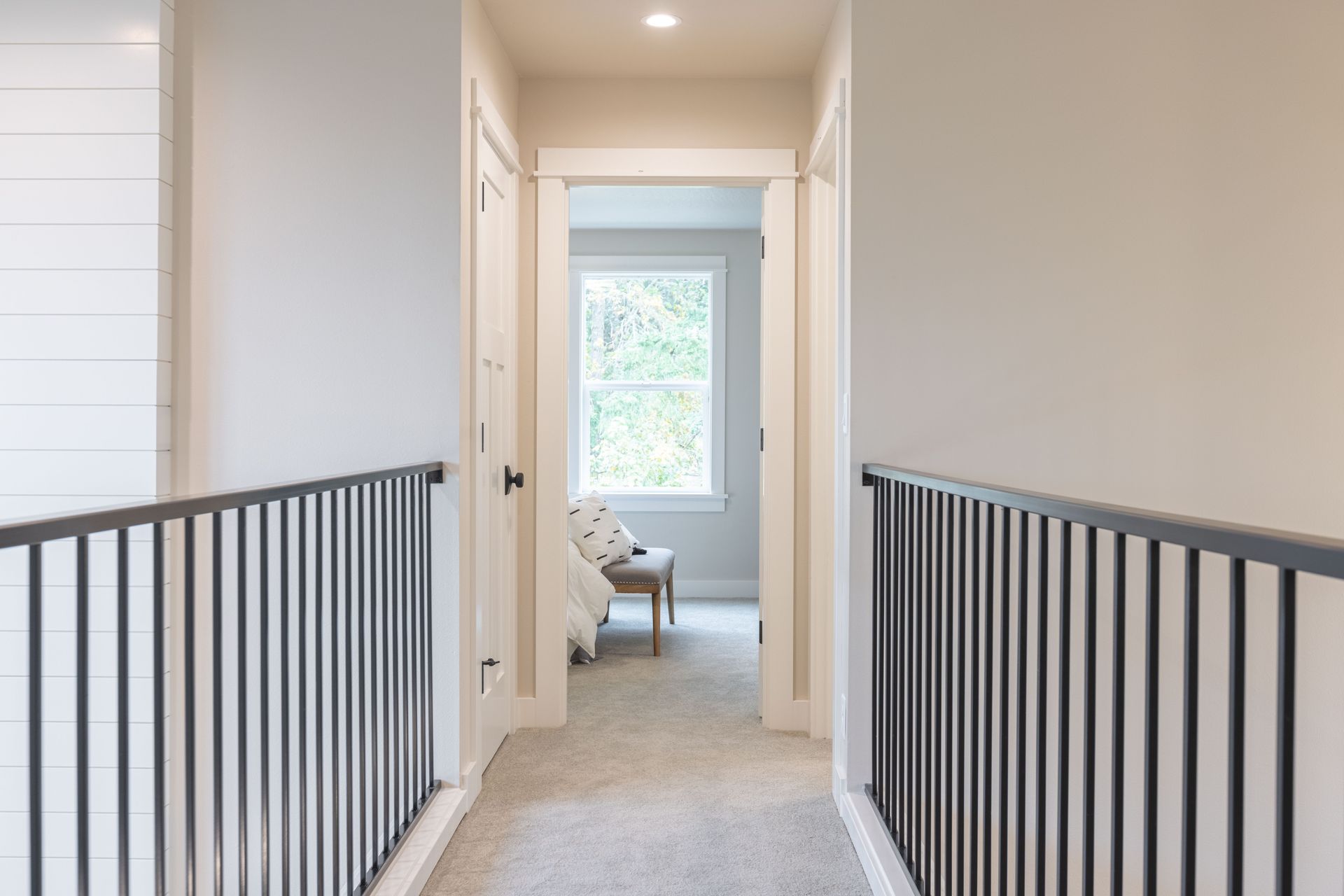 White hallway with black railing, leading to a bright room and window at the end