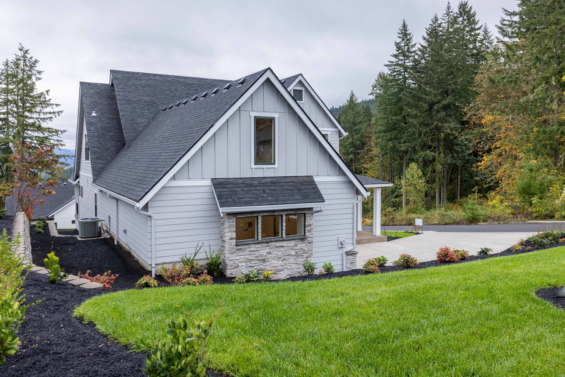 Gray house with steep roof and manicured green lawn surrounded by trees and shrubs