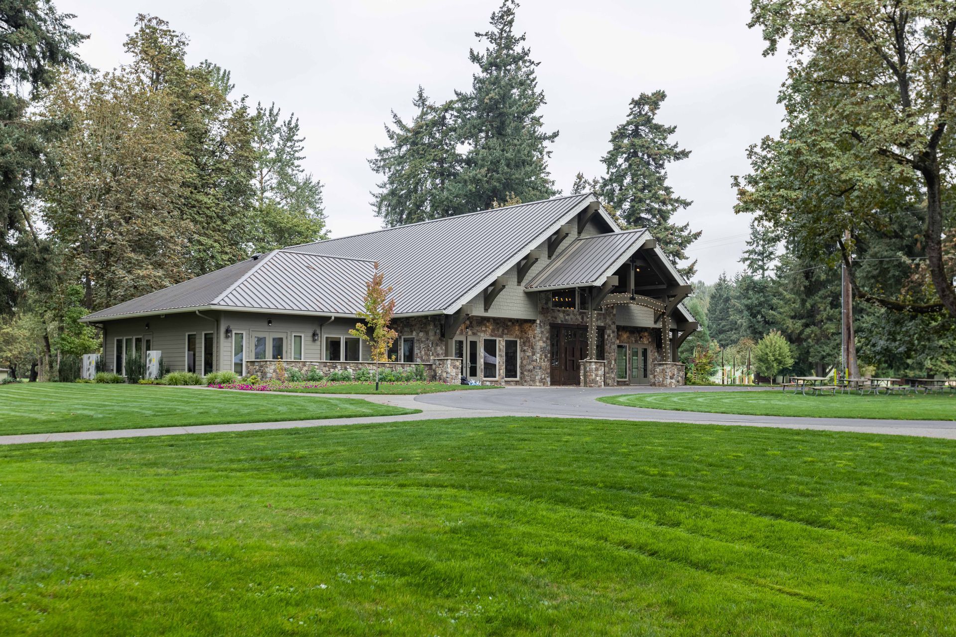 Stone house with a gray roof on a green lawn, surrounded by tall trees.