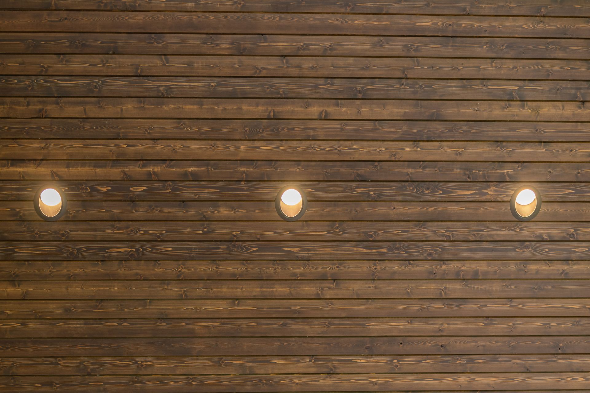Three warm lights hanging against a rustic wooden plank wall