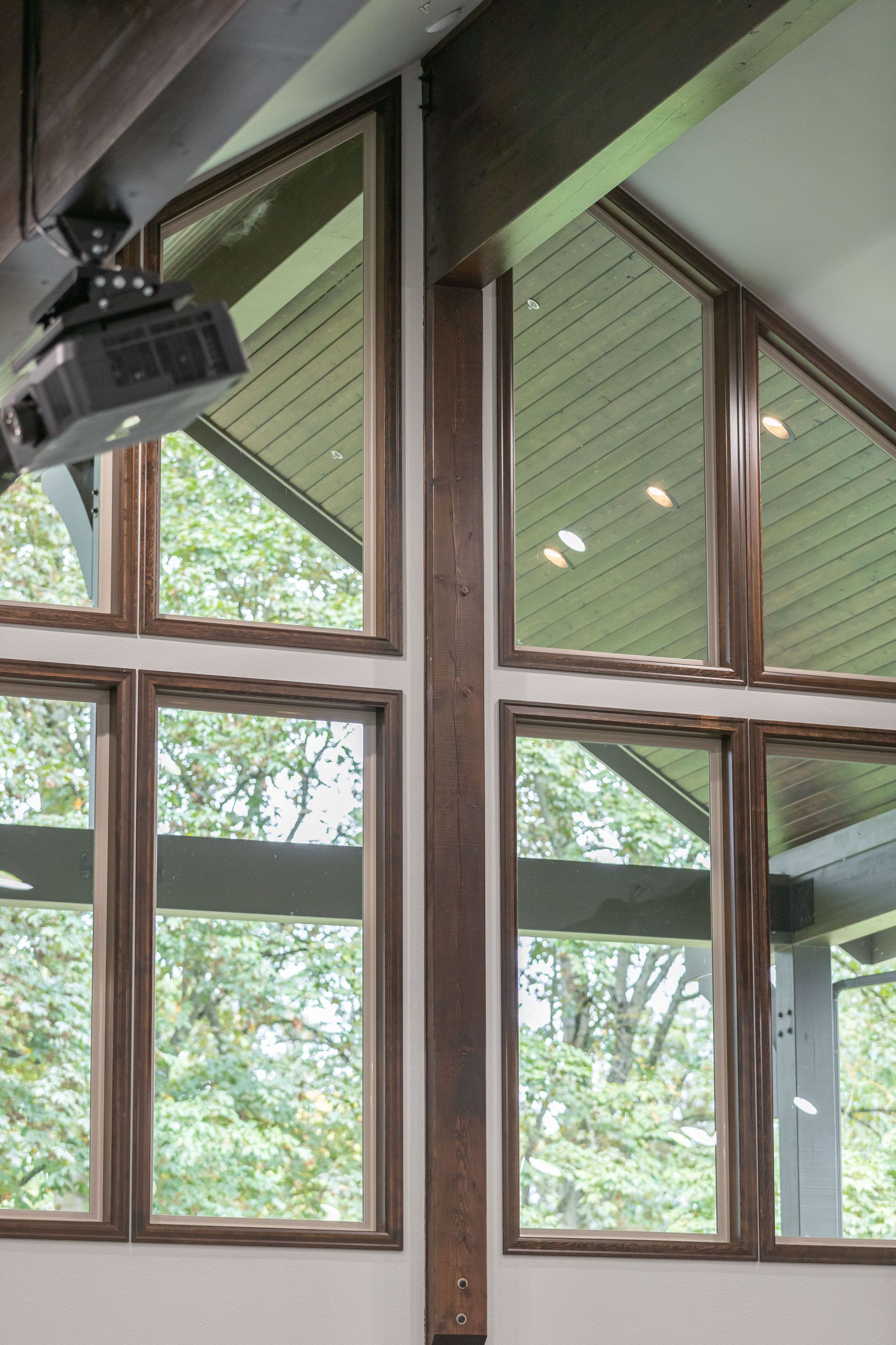 Large windows with dark wood frames under a slanted ceiling, showing green trees outside