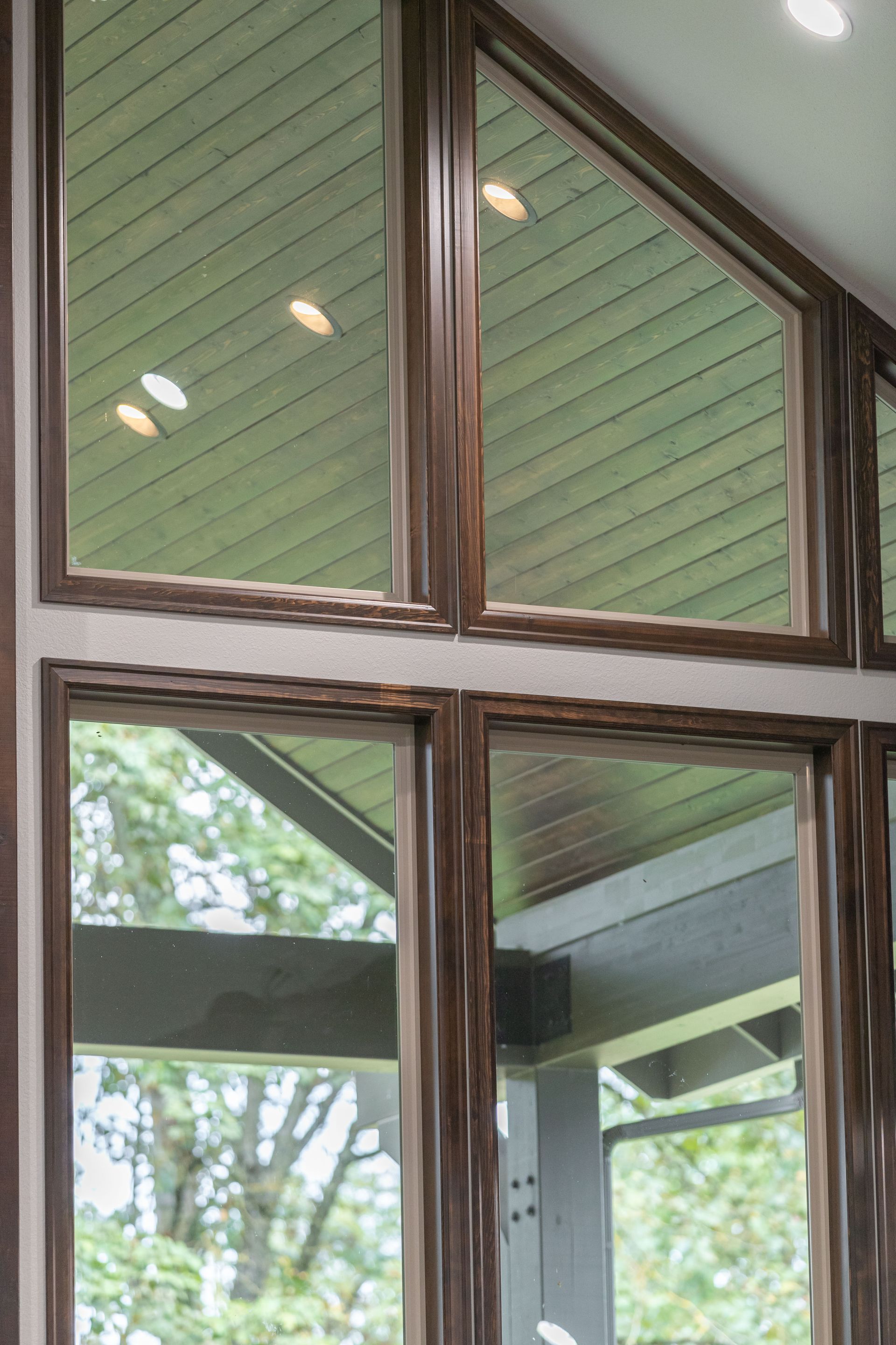 Window with dark wood trim and triangular panes, reflecting a green roof and trees outside.