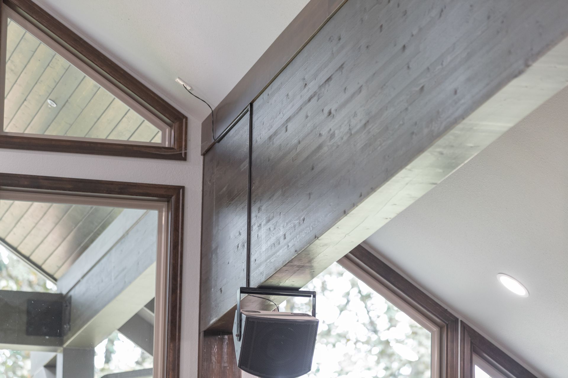 Interior view of a modern room with large triangular windows, exposed wood beams, and a hanging black speaker.