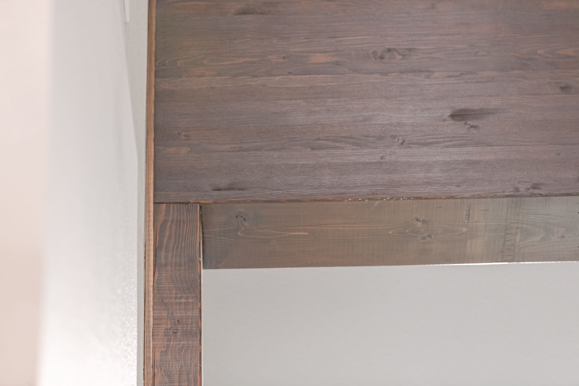 Close-up of a wooden furniture corner with gray-brown grain against a white wall.