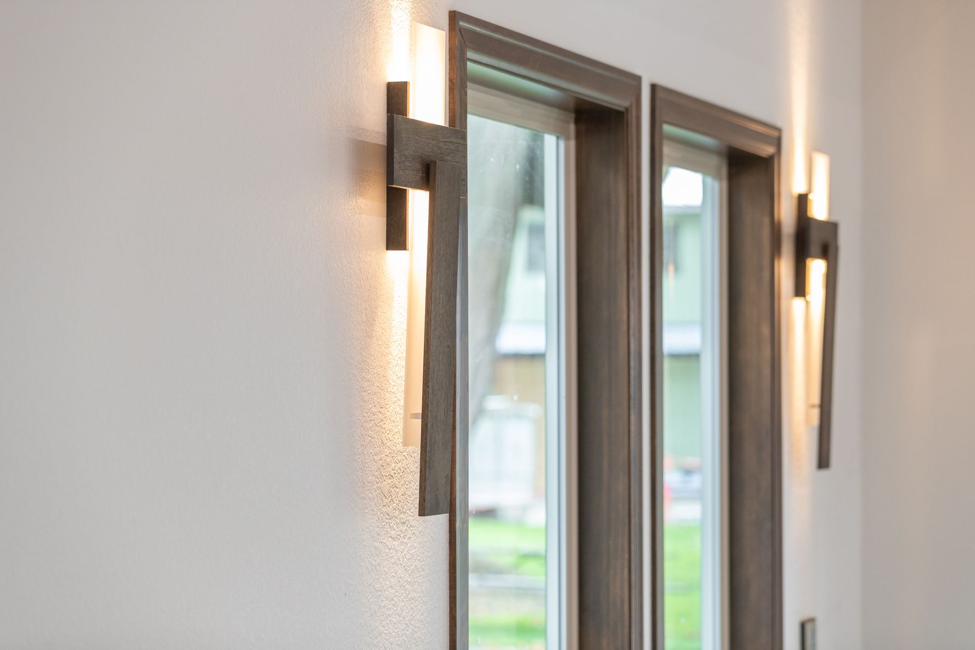 Modern wall sconces flanking a tall window in a bright interior hallway