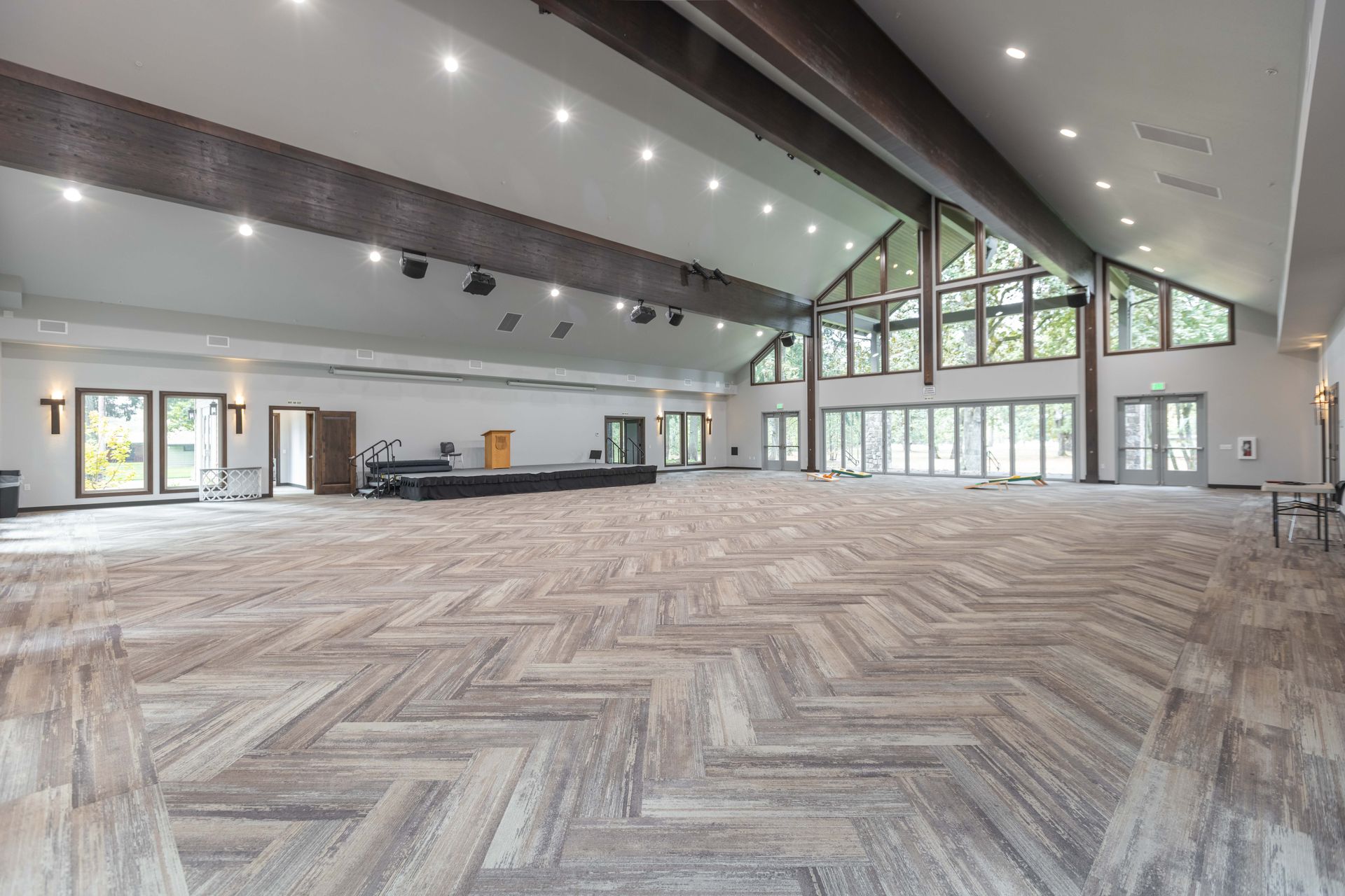 Spacious modern hall with herringbone wood flooring, tall windows, and white walls under a high ceiling
