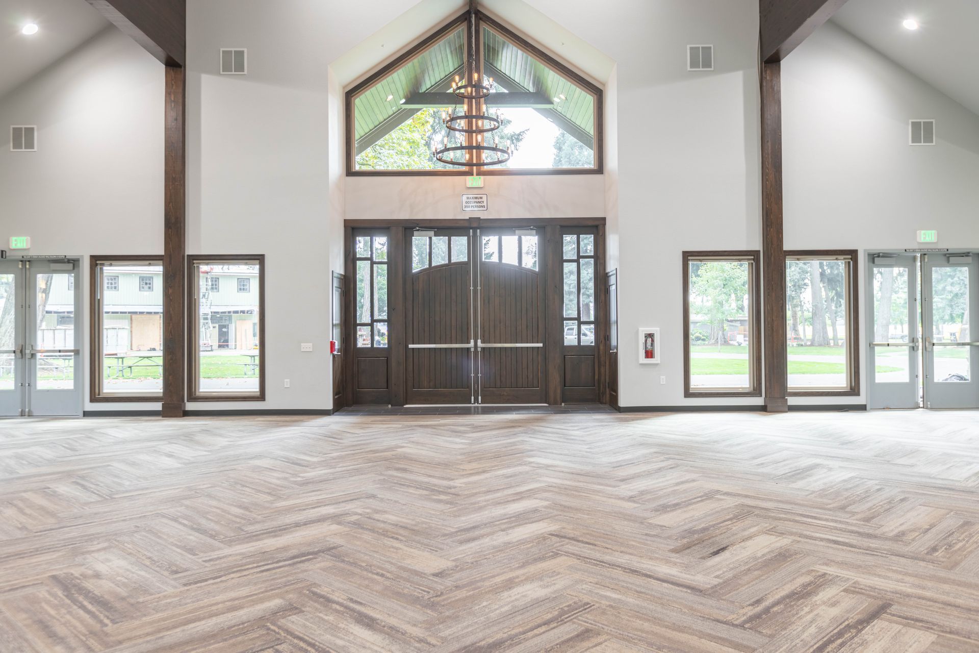 Bright empty lobby with vaulted ceiling, glass doors, and herringbone wood floor