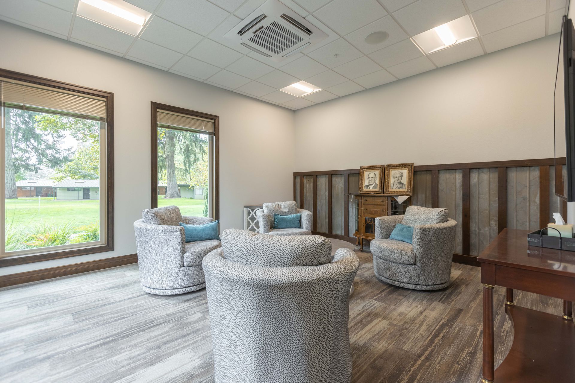 Bright waiting room with gray chairs, wood flooring, cabinets, and large windows.