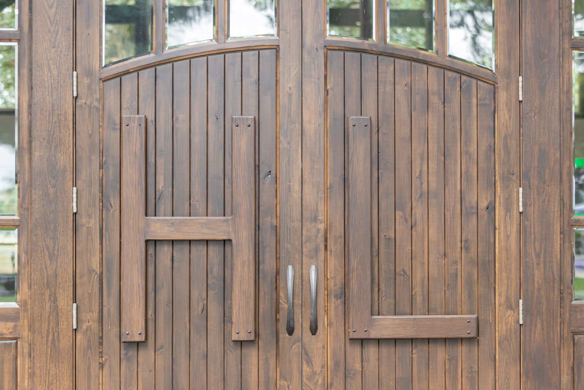 Wooden garden gate with arched top and small window panes in a rustic fence