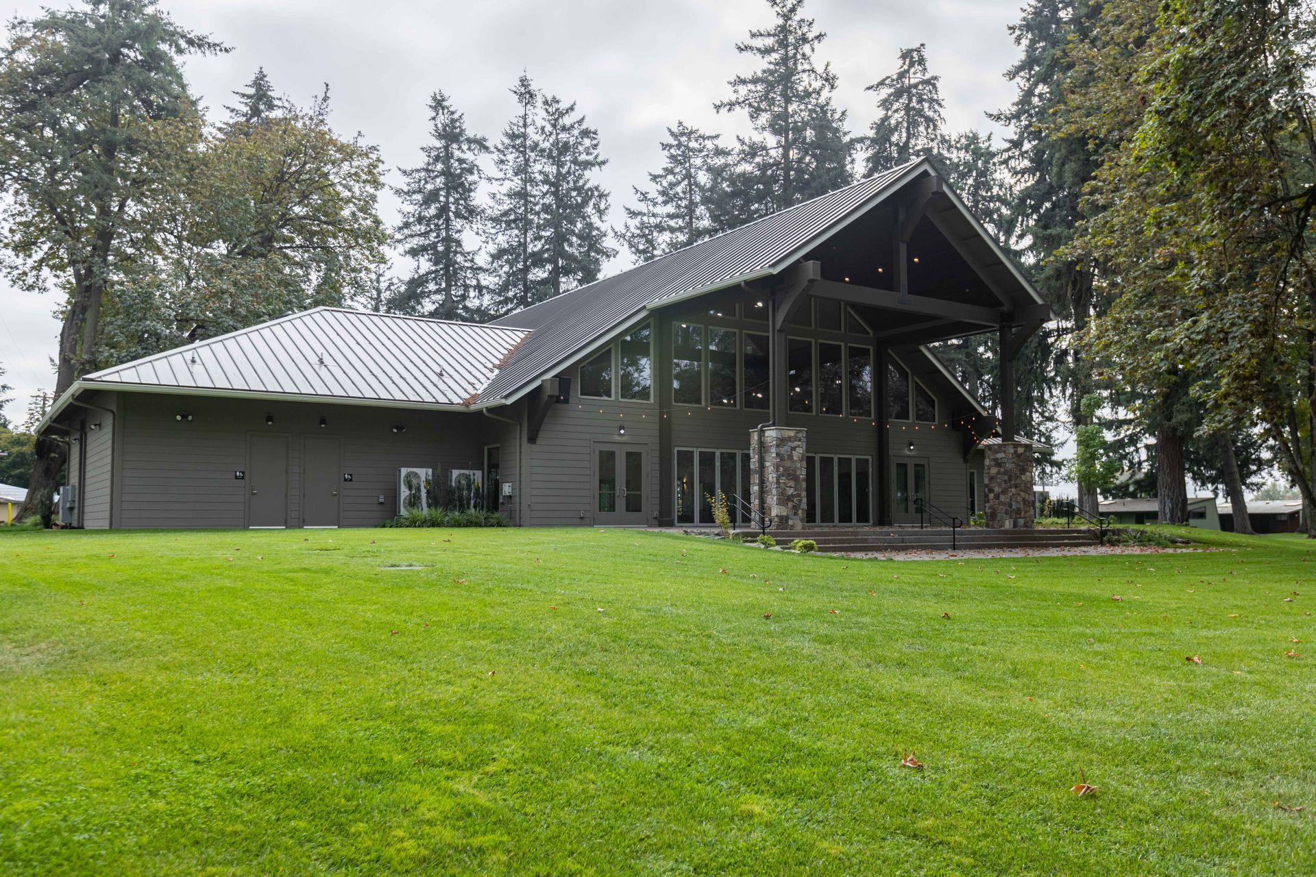Modern lodge-style building with large windows and a green lawn, surrounded by trees