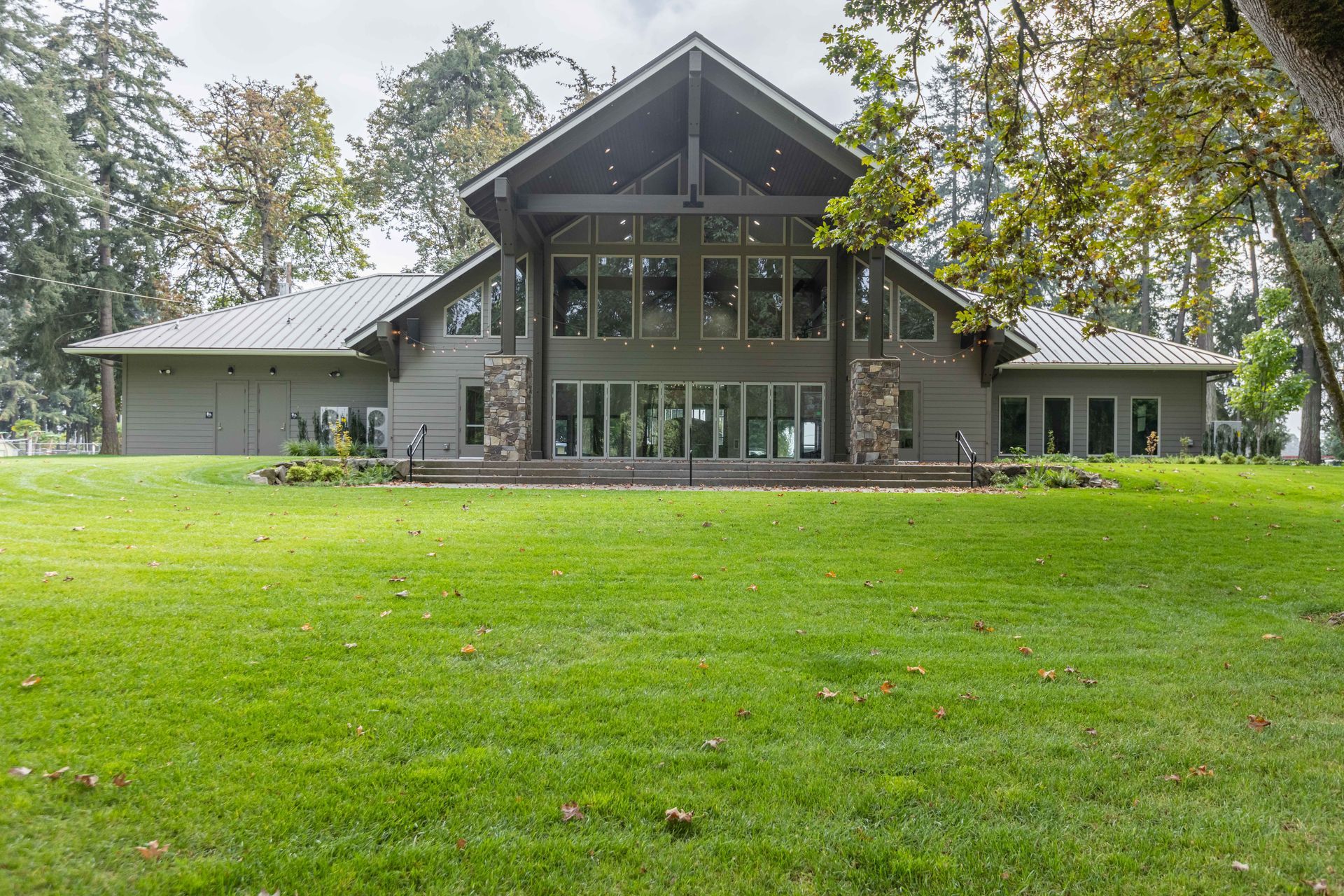 Large modern house with a glass front, centered on a wide green lawn and surrounded by trees