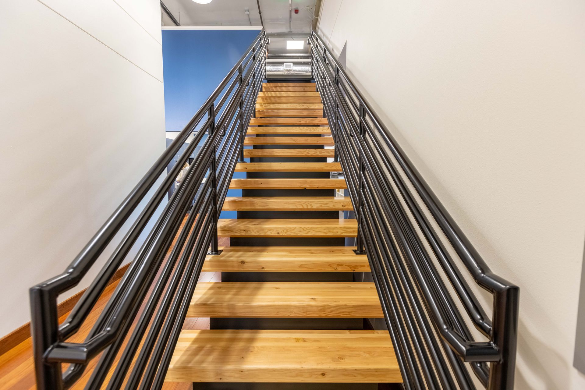 Interior staircase with wooden steps, black railings, and white walls, viewed from the bottom up