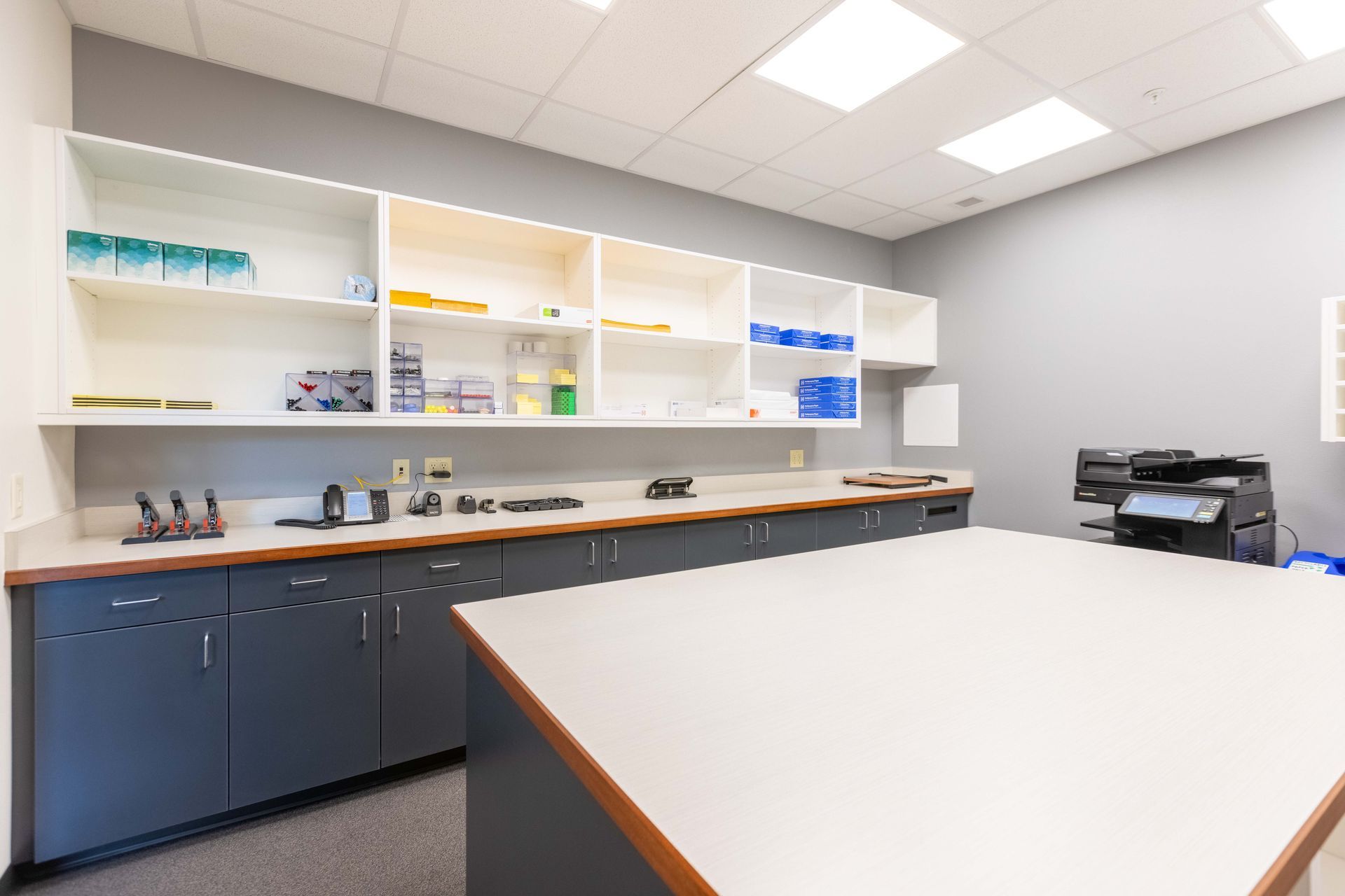 Modern office break room with white cabinets, dark lower cabinets, countertop, printer, and table