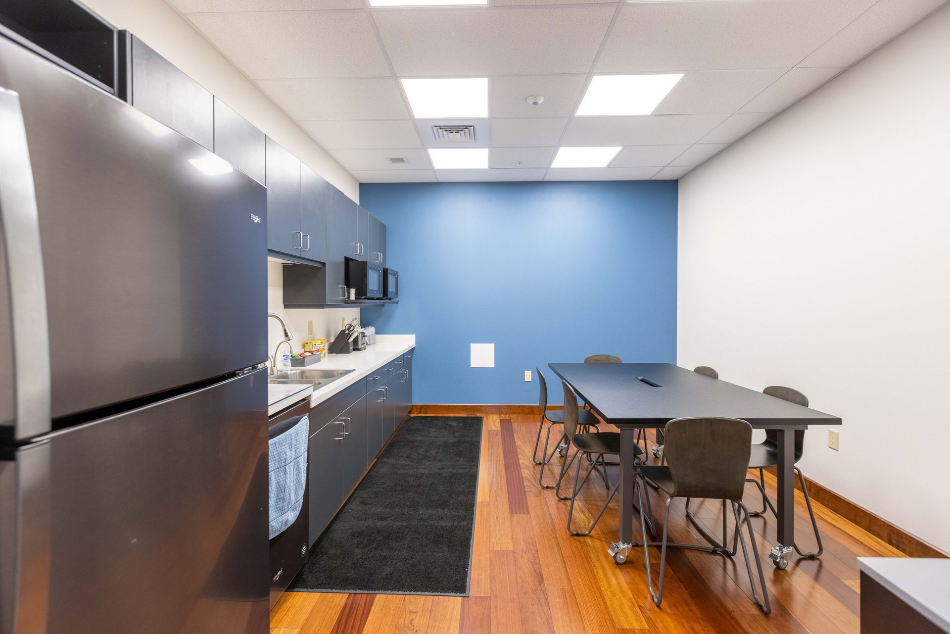Modern office kitchenette with stainless fridge, blue wall, counter, and meeting table with chairs