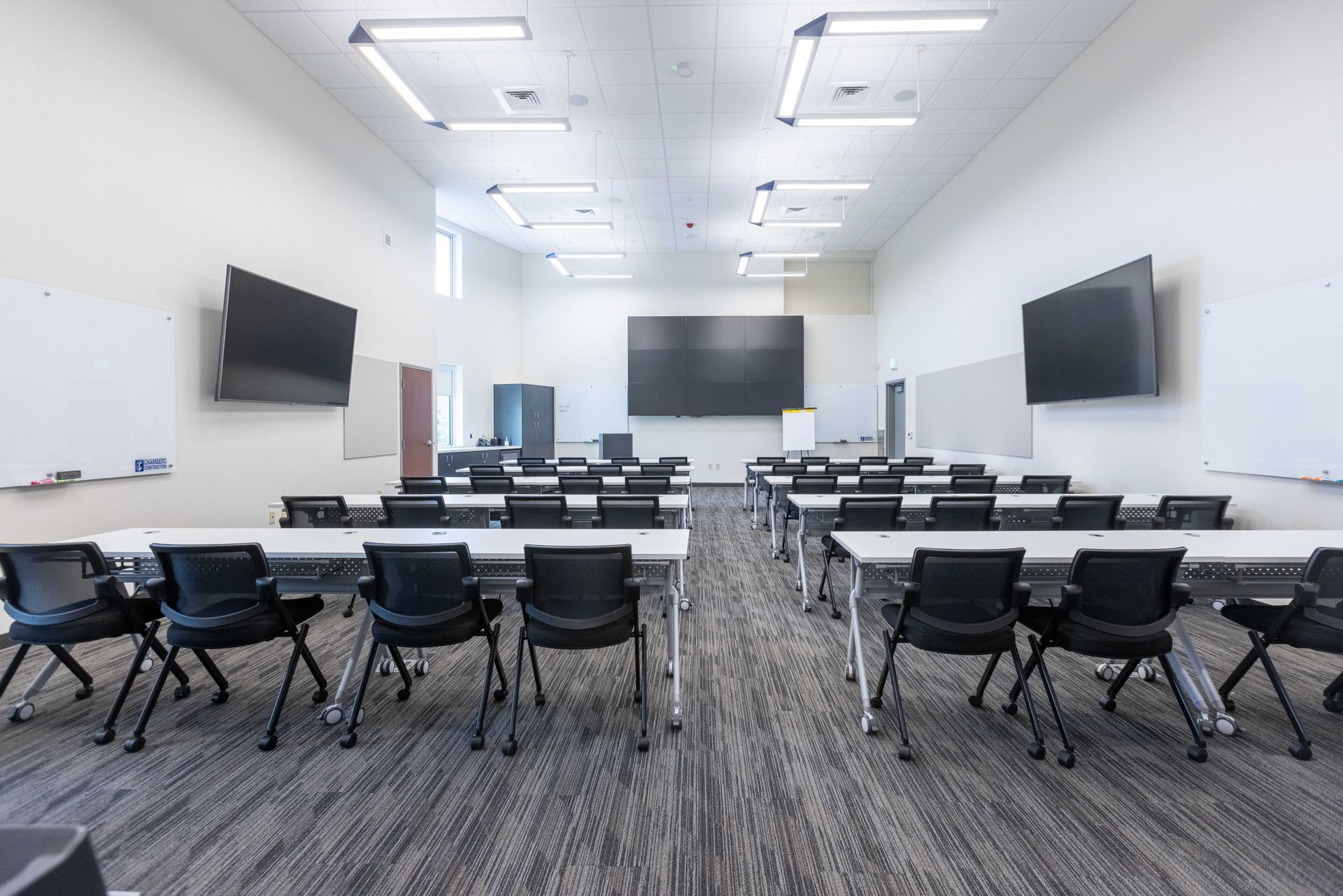 Empty modern classroom with rows of desks, large wall screens, and bright overhead lights