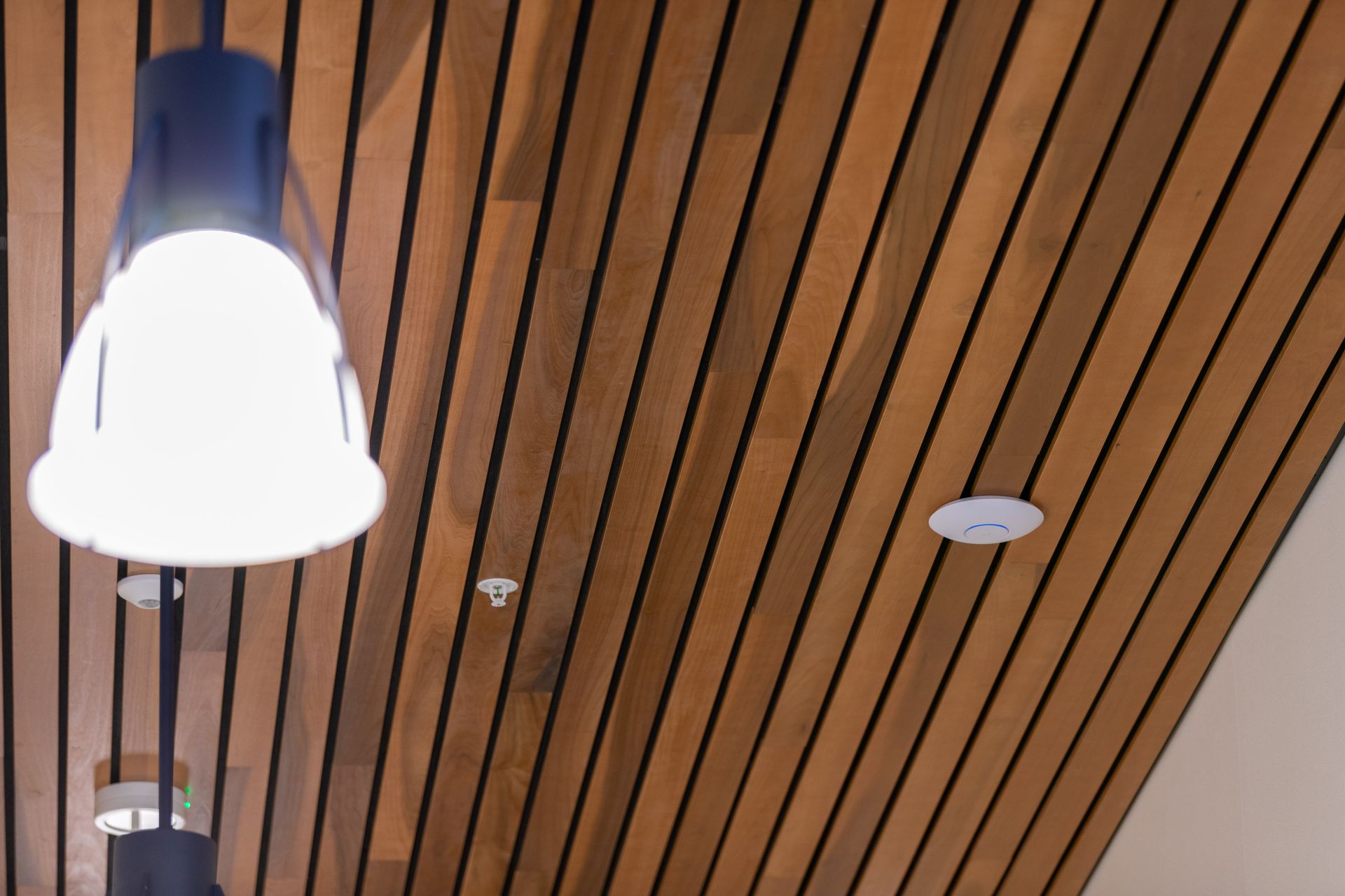 Wood slat ceiling with hanging white pendant light and a round recessed speaker or vent