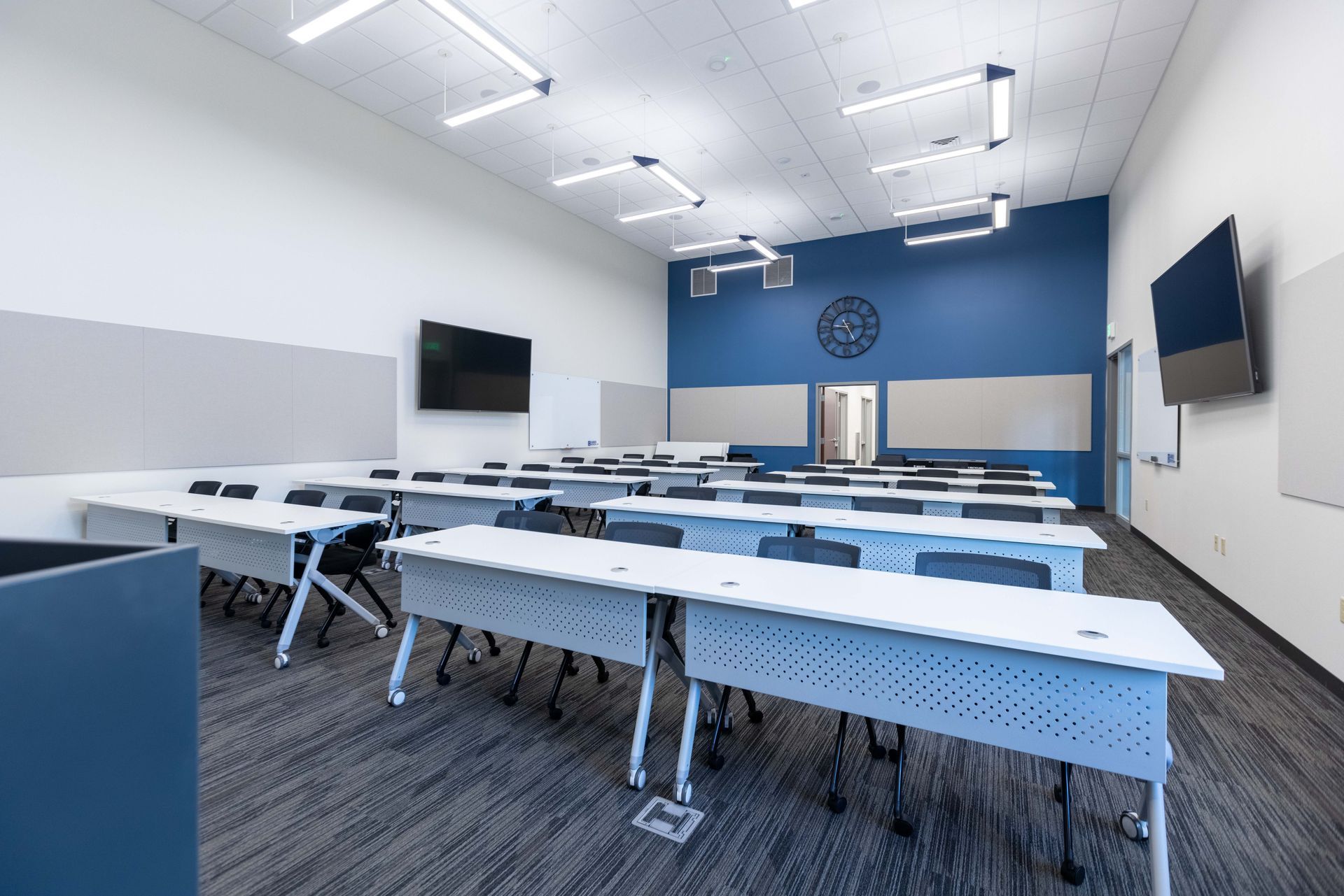 Empty modern classroom with rows of desks, blue accent wall, and wall-mounted screens