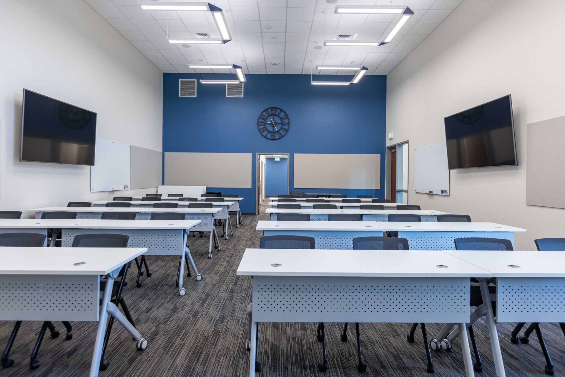 Empty modern classroom with rows of desks, wall-mounted screens, and a blue accent wall