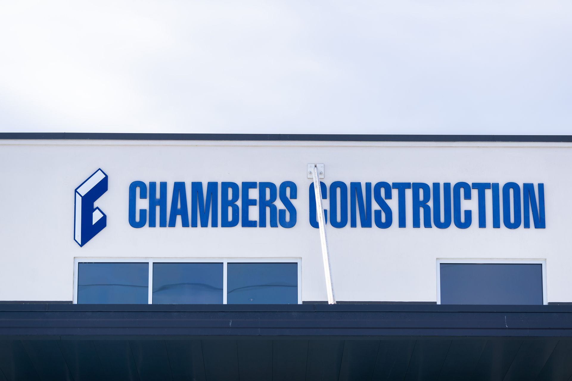 Blue “Chambers Construction” sign on a building roof against a cloudy sky