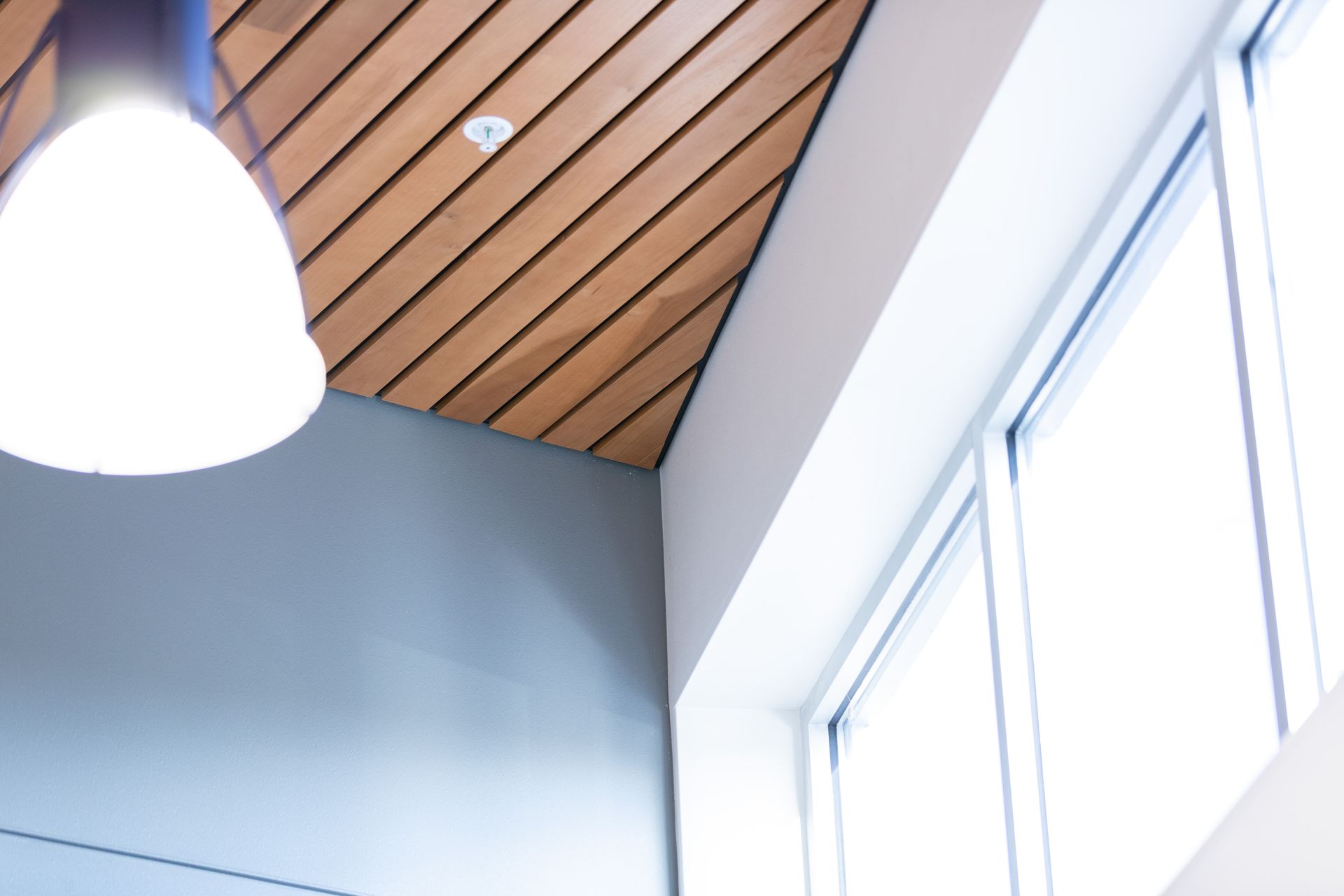 White pendant light and wood slat ceiling beside tall windows in a bright room