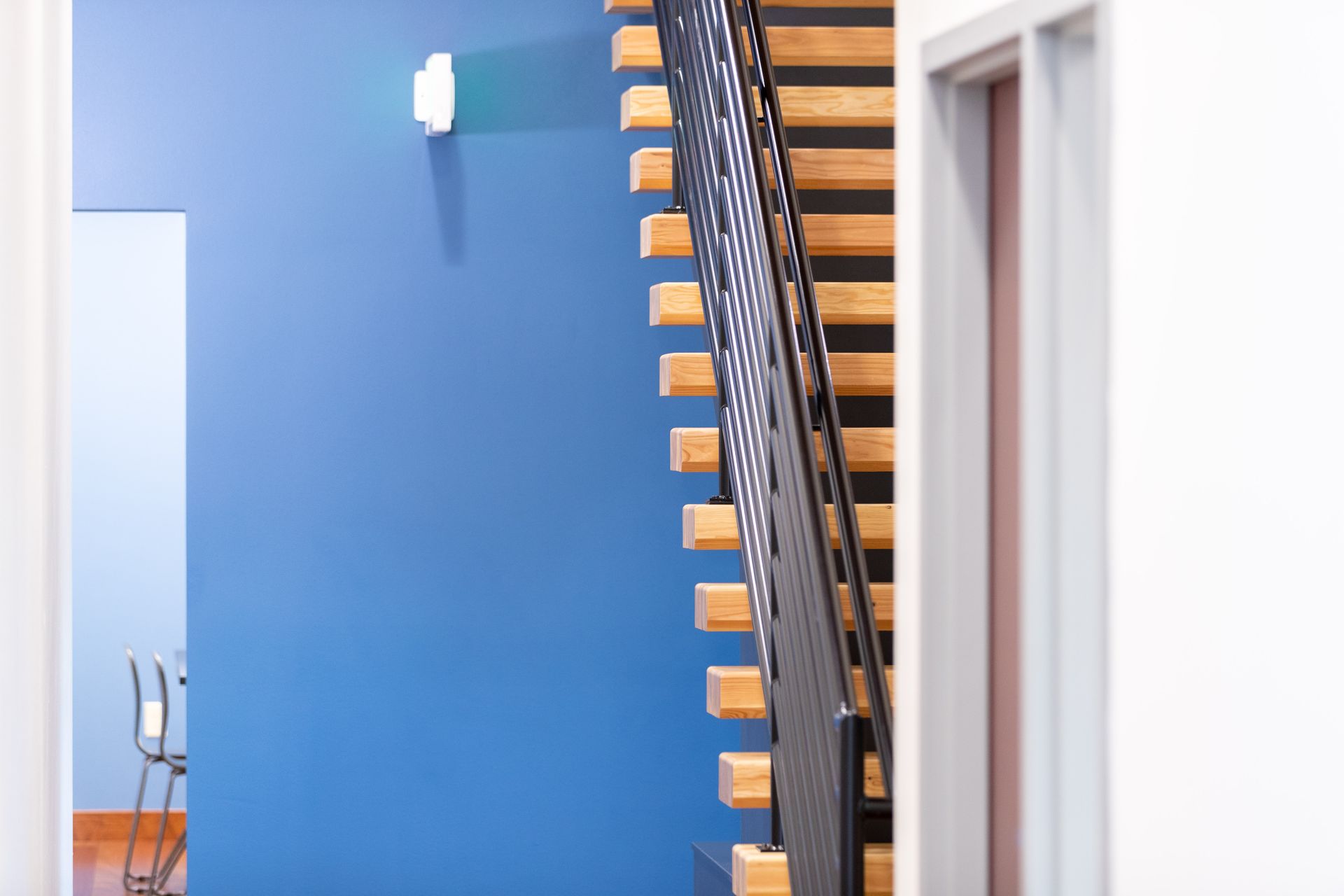 Modern staircase with black railing against a bright blue wall in a white interior corridor