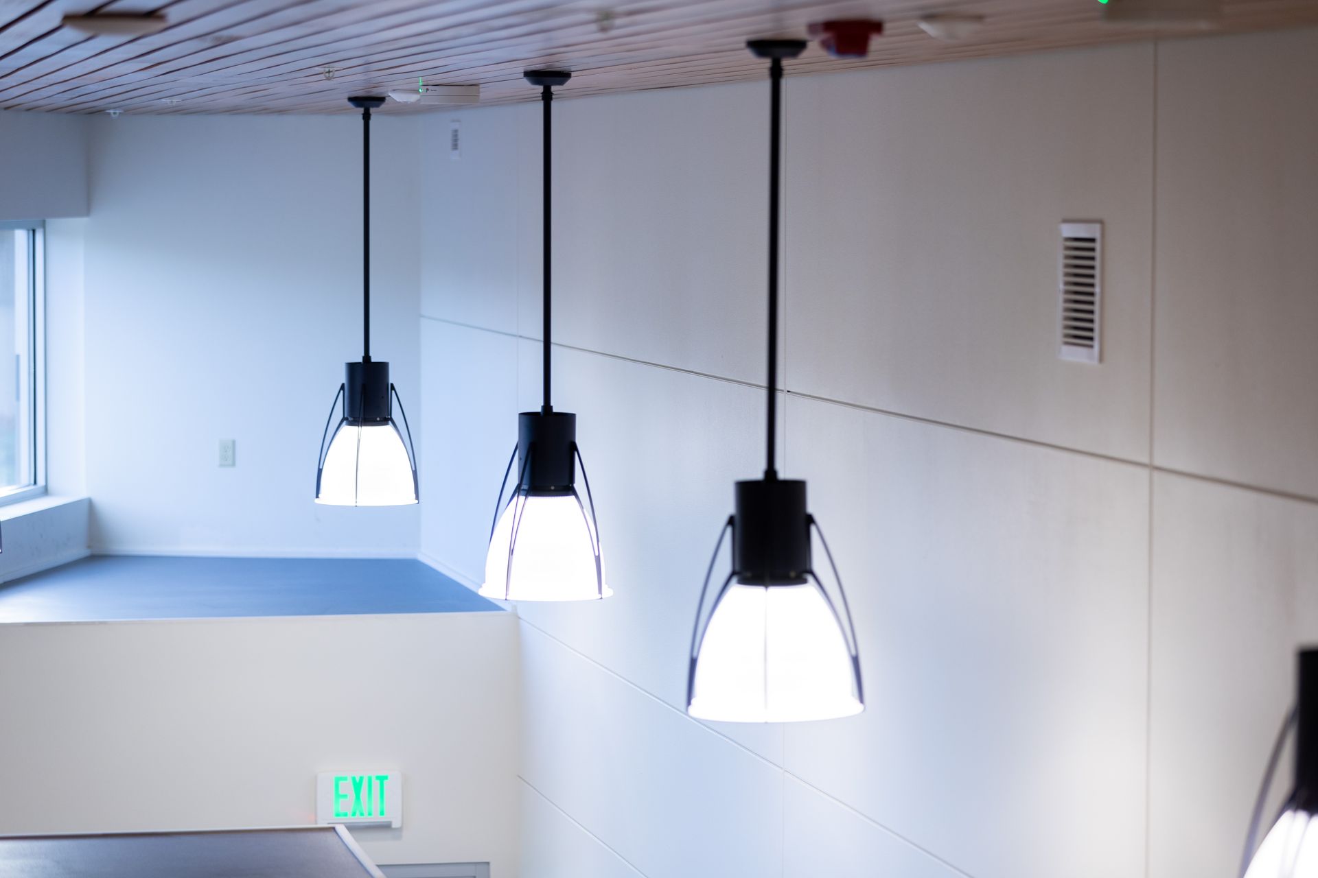 Three black pendant lights hanging from a white ceiling in a modern interior hallway