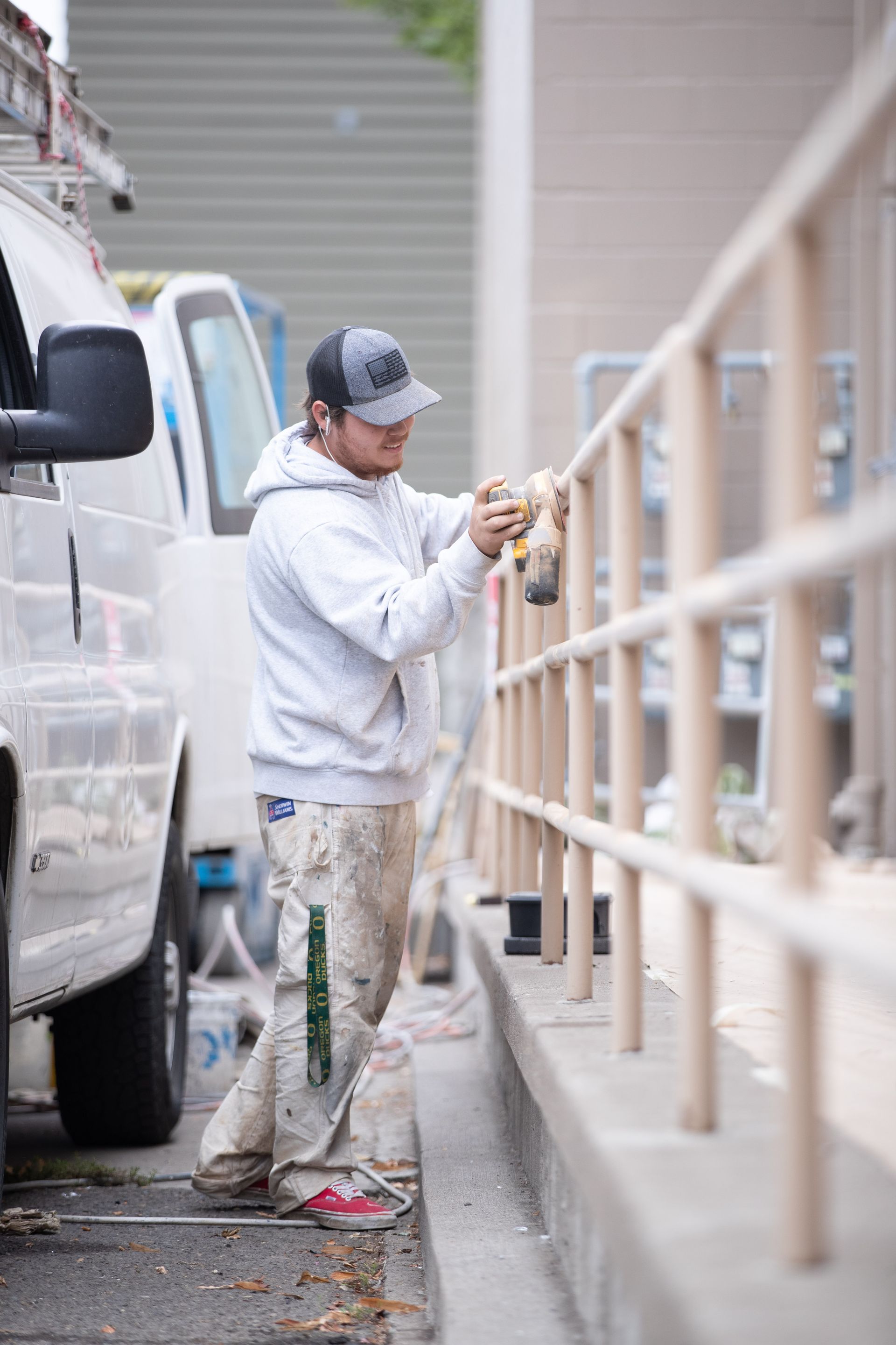 Person painting a beige railing beside a white van in an outdoor alley.